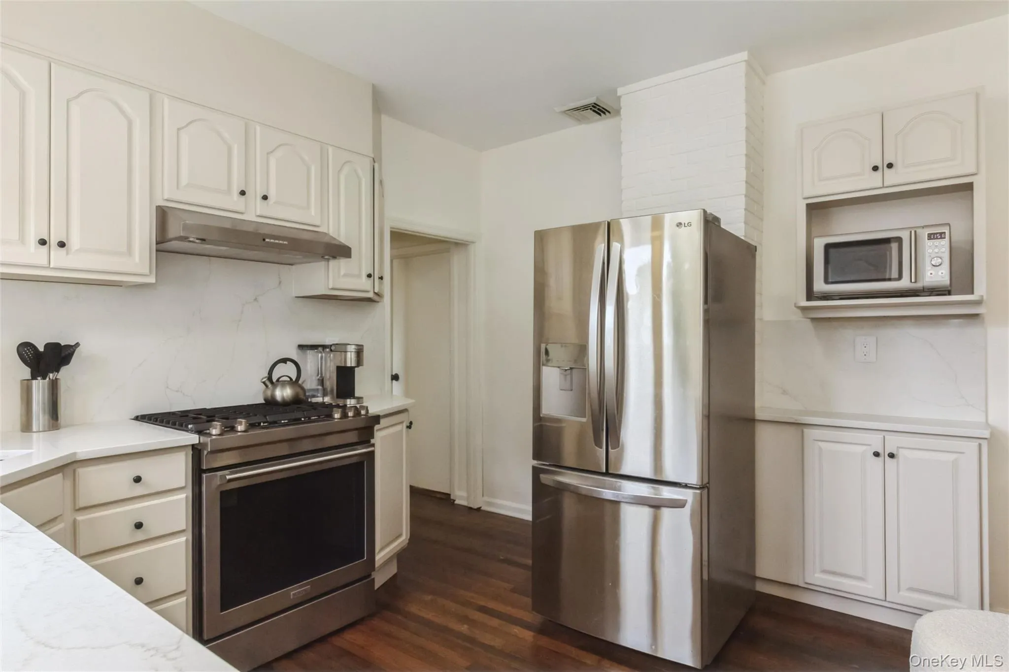 Kitchen featuring wood-finish flooring, white cabinetry, integrated stainless steel appliances, and white countertops with matching backsplashes Kitchen featuring wood-finish flooring, white cabinetry, integrated stainless steel appliances, and white countertops with matching backsplashes