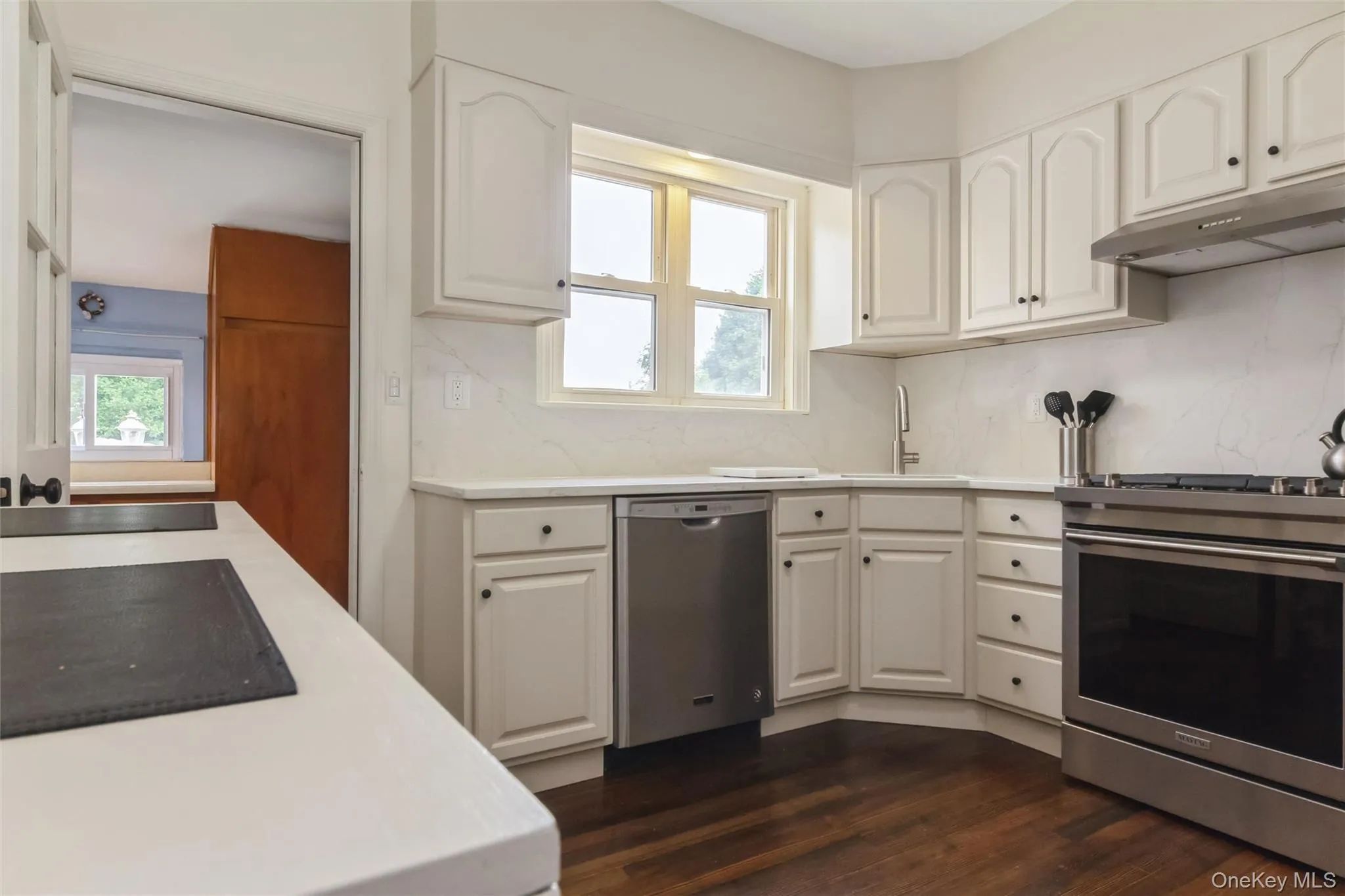 Kitchen featuring white cabinetry, light countertops, wood-finish flooring, stainless steel appliances, and a window above the sink Kitchen featuring white cabinetry, light countertops, wood-finish flooring, stainless steel appliances, and a window above the sink