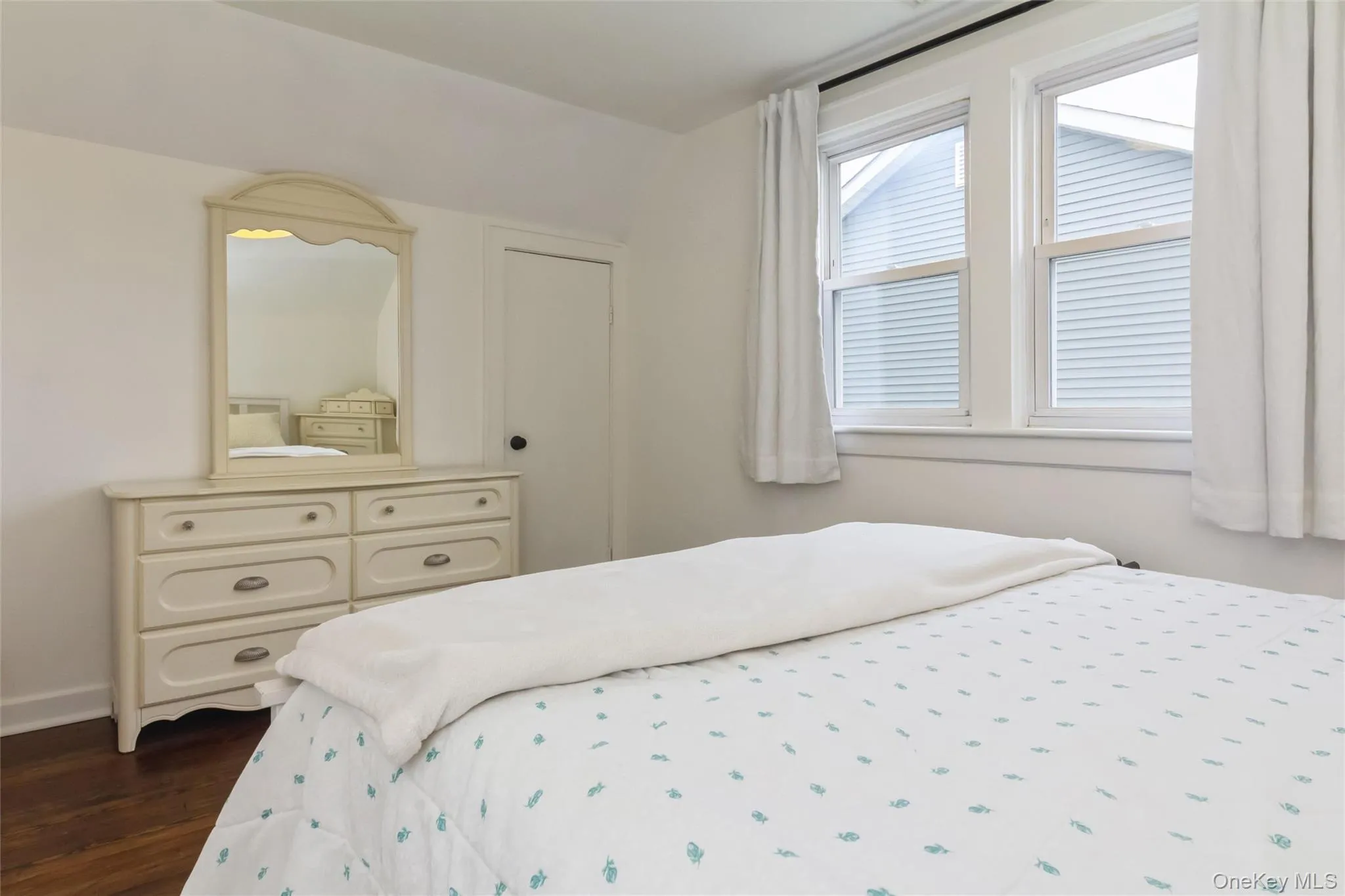 Bedroom featuring wood-finish flooring, white walls, and dual window openings Bedroom featuring wood-finish flooring, white walls, and dual window openings