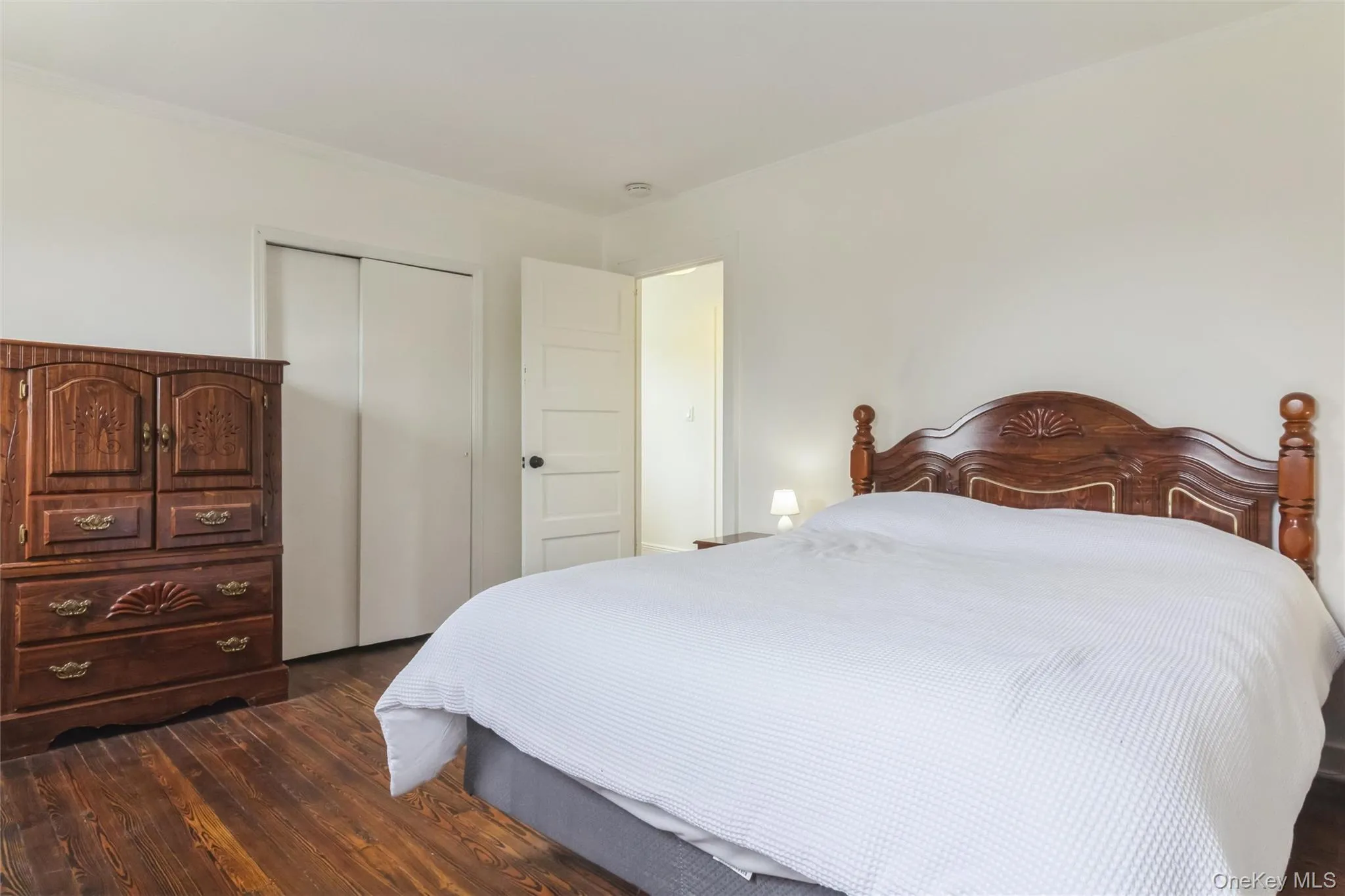 Bedroom featuring wood-finish flooring, white walls, and a sliding door closet Bedroom featuring wood-finish flooring, white walls, and a sliding door closet
