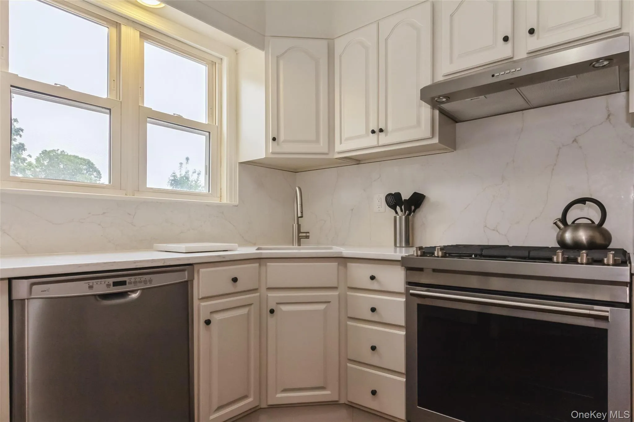 Kitchen featuring white cabinetry, light countertops, and a white and grey veined backsplash Kitchen featuring white cabinetry, light countertops, and a white and grey veined backsplash
