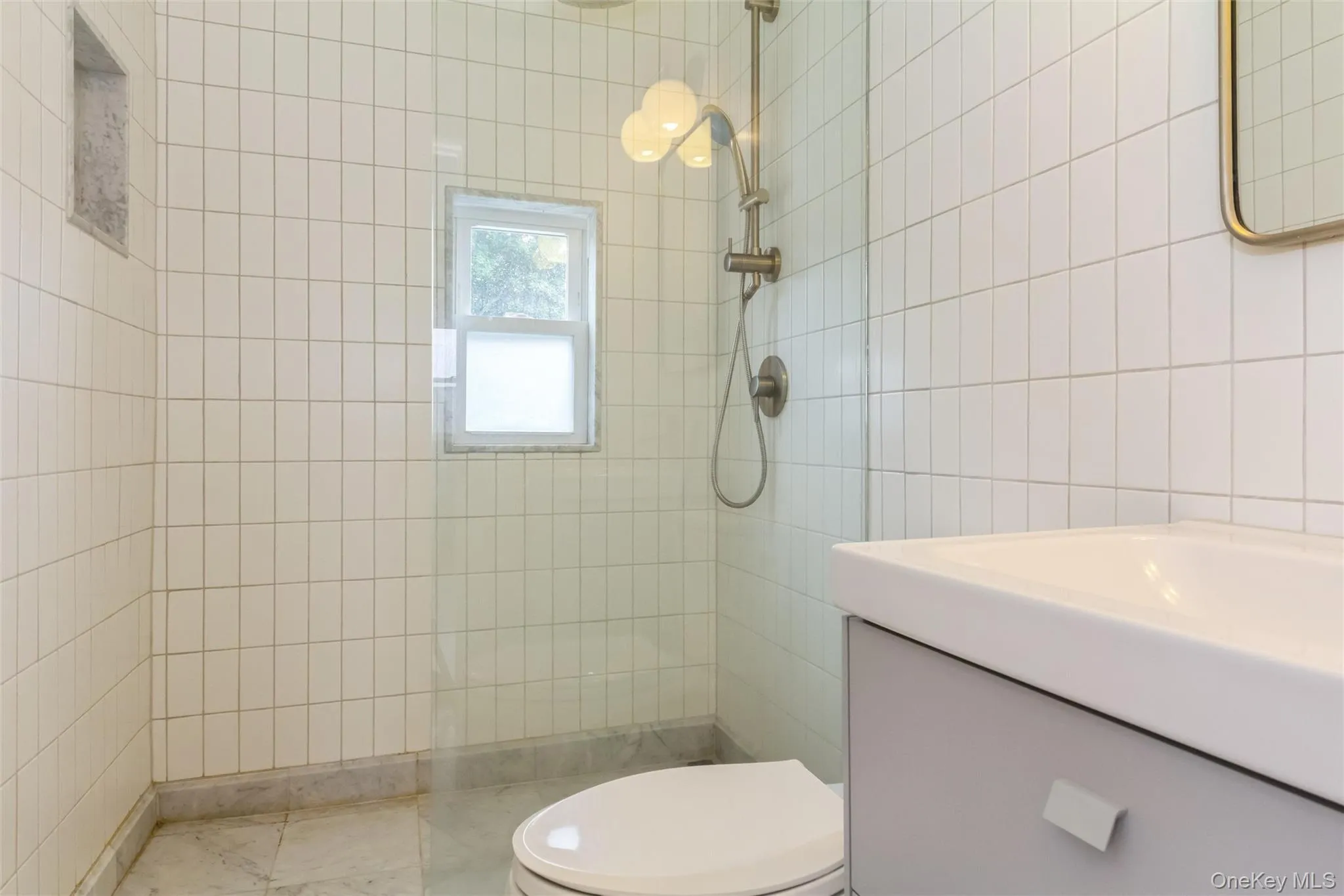 Contemporary bathroom featuring vertical subway tile walls, a glass shower enclosure, a built-in shower niche, and a window providing natural light Contemporary bathroom featuring vertical subway tile walls, a glass shower enclosure, a built-in shower niche, and a window providing natural light