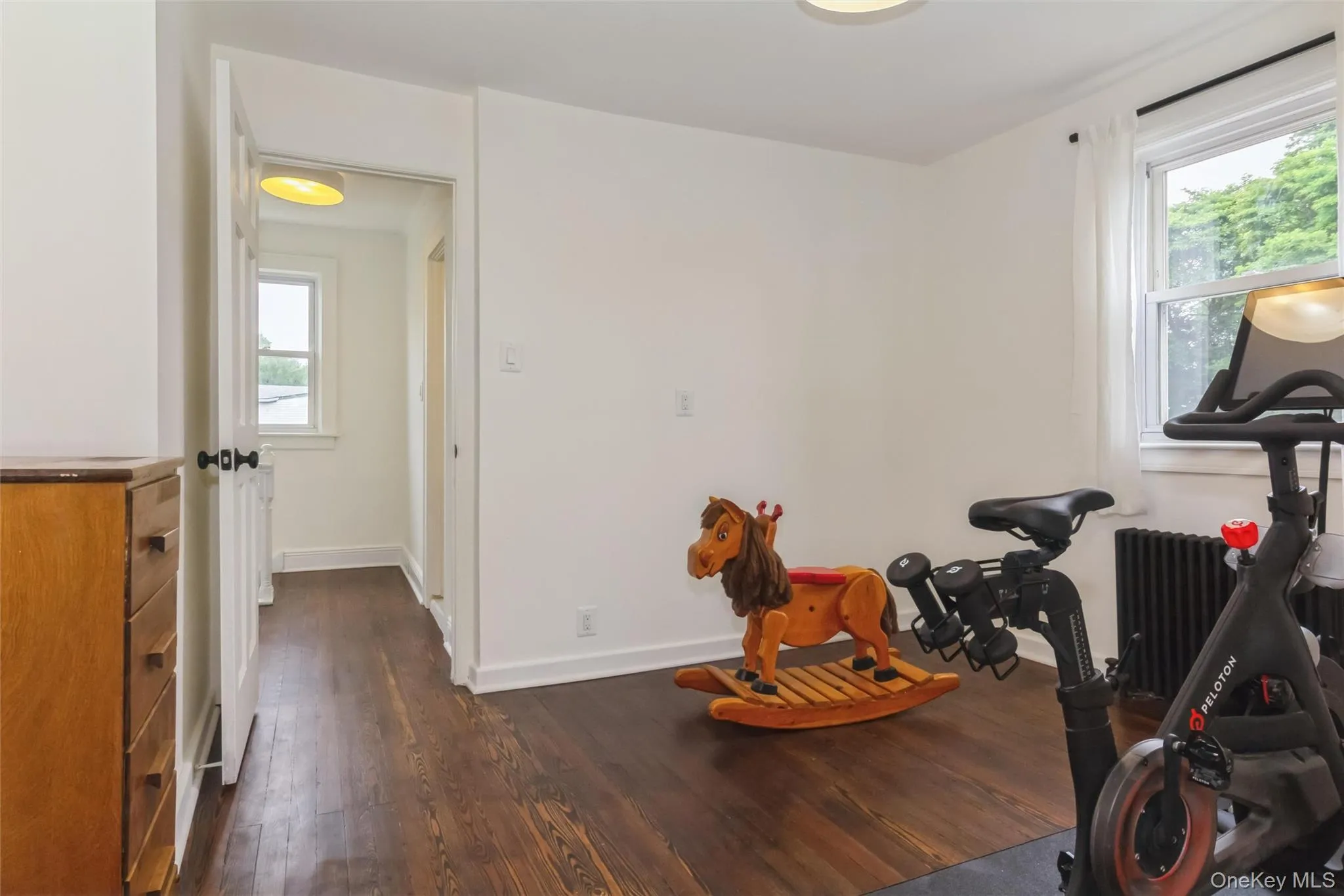 Bright room with dark wood-finish flooring, white walls, and a visible window Bright room with dark wood-finish flooring, white walls, and a visible window