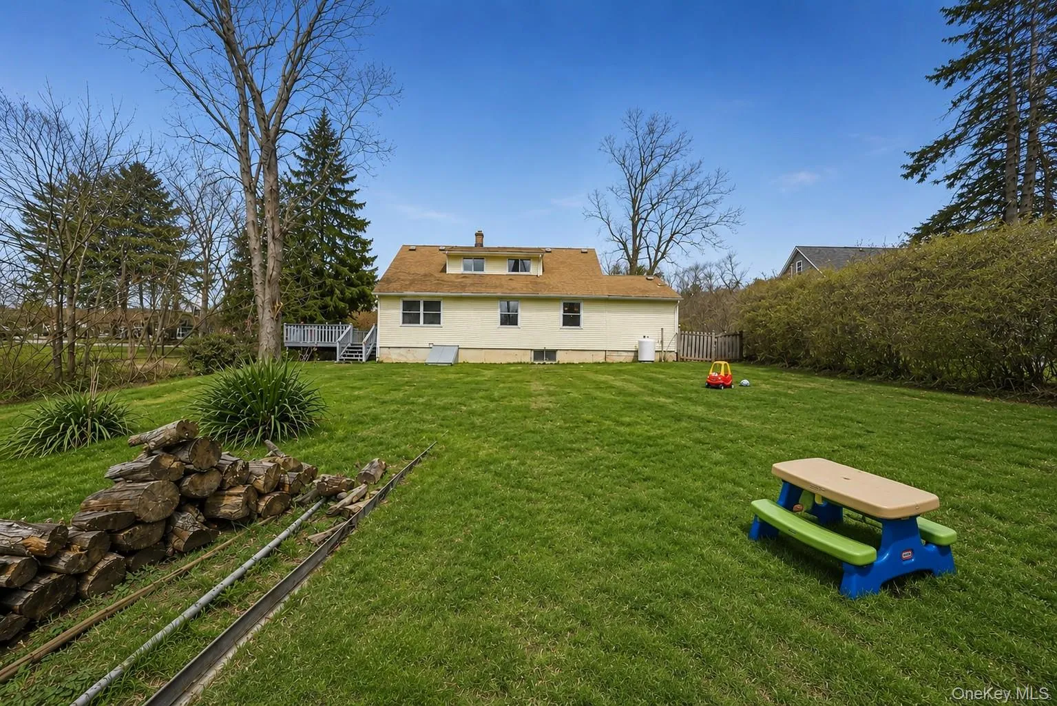 Expansive green lawn with mature trees and a rear house exterior featuring a deck with stairs Expansive green lawn with mature trees and a rear house exterior featuring a deck with stairs