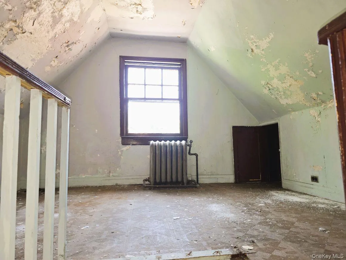 Attic- front room space featuring an operable window with wood trim, a vintage-style radiator, and a built-in storage door Attic- front room space featuring an operable window with wood trim, a vintage-style radiator, and a built-in storage door