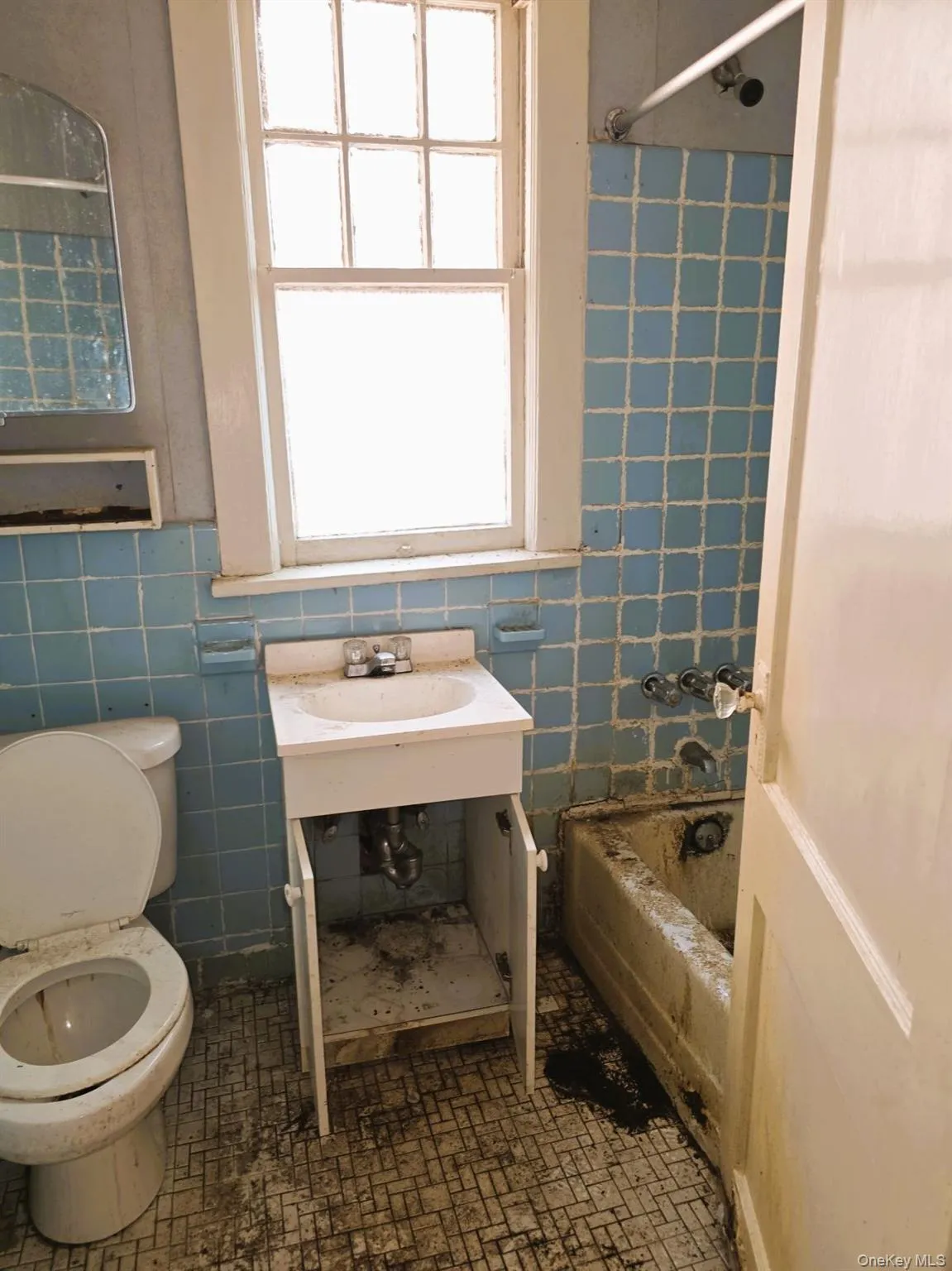 Bathroom featuring a window, tile flooring, a toilet, a vanity with a sink, and a bathtub with tiled walls Bathroom featuring a window, tile flooring, a toilet, a vanity with a sink, and a bathtub with tiled walls