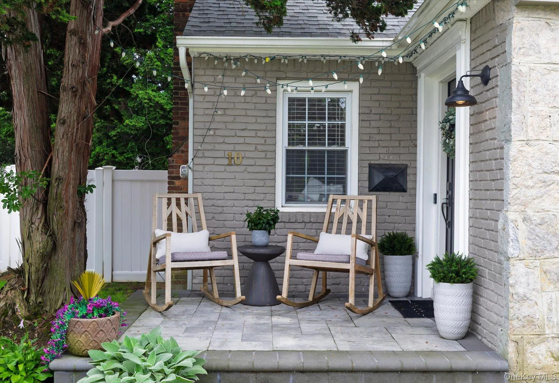 Front entryway with a paver patio, brick facade, stone accents, and a white vinyl fence Front entryway with a paver patio, brick facade, stone accents, and a white vinyl fence