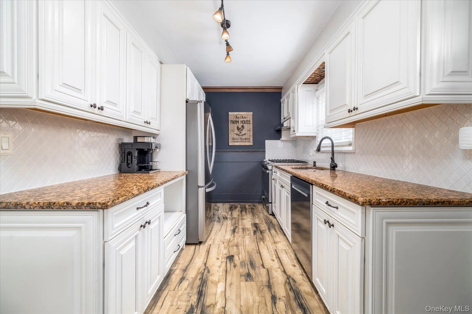 Renovated kitchen featuring white cabinetry, wood-finish flooring, and stone countertops Renovated kitchen featuring white cabinetry, wood-finish flooring, and stone countertops