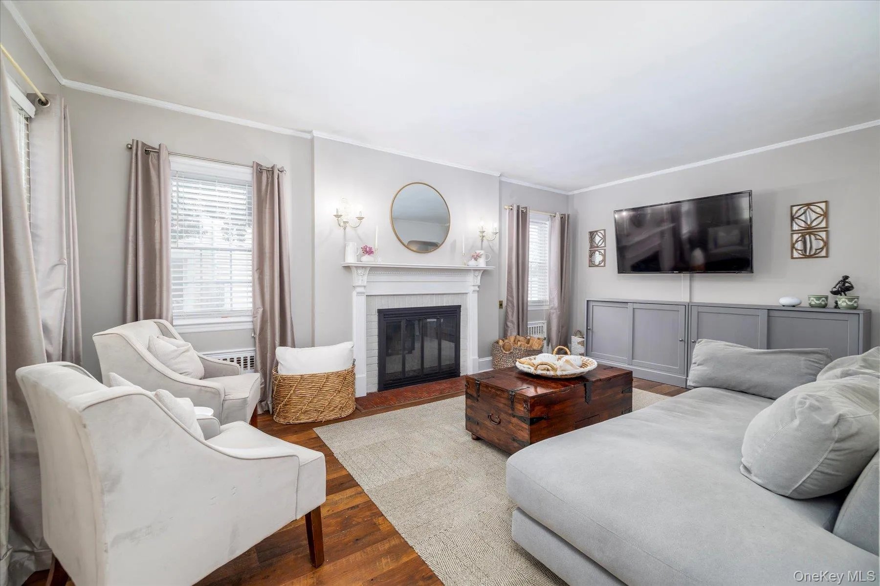 Living room featuring hardwood flooring and a wood burning fireplace with a white mantel and hearth Living room featuring hardwood flooring and a wood burning fireplace with a white mantel and hearth