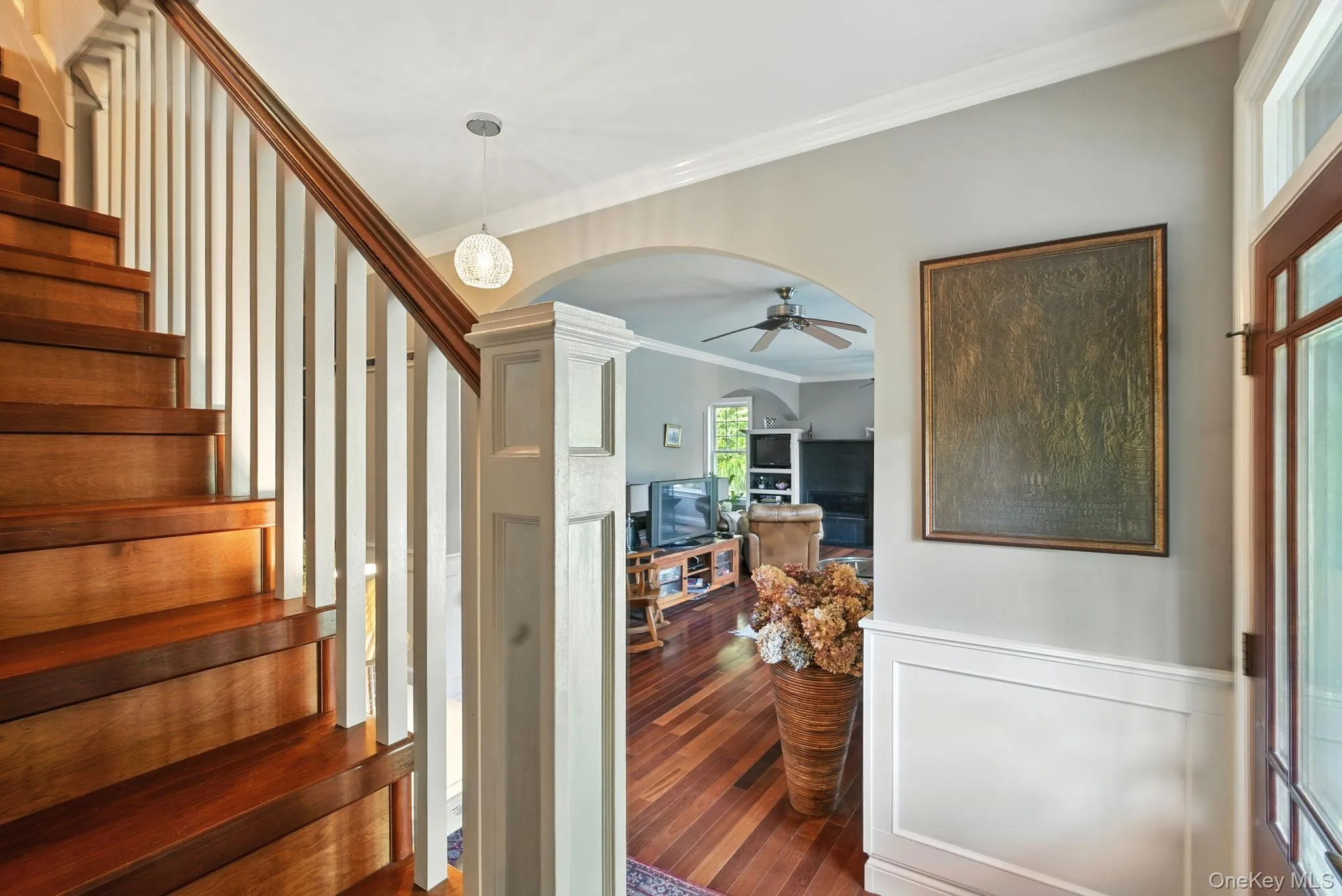 Staircase with crown molding, arched walkways, a ceiling fan, wood-type flooring, and wainscoting Staircase with crown molding, arched walkways, a ceiling fan, wood-type flooring, and wainscoting