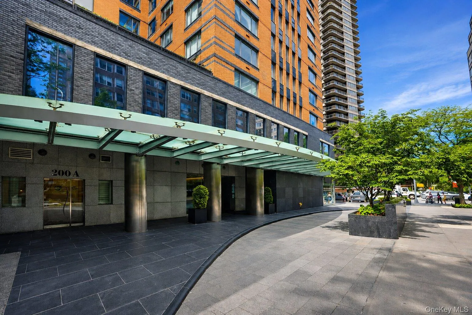 Building entrance featuring a glass canopy, large format stone-finish tile, stone-clad facade, and a modern brick-and-glass tower Building entrance featuring a glass canopy, large format stone-finish tile, stone-clad facade, and a modern brick-and-glass tower