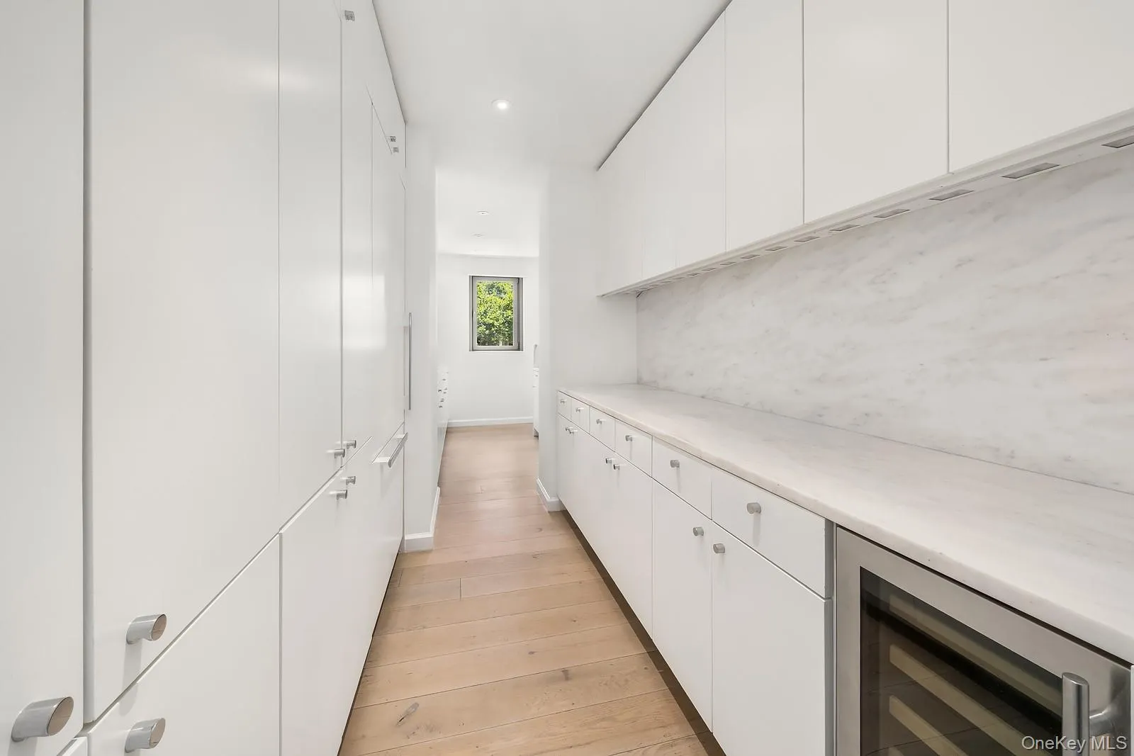 Galley-style kitchen featuring abundant white cabinetry, light wood-finish flooring, and integrated appliances Galley-style kitchen featuring abundant white cabinetry, light wood-finish flooring, and integrated appliances