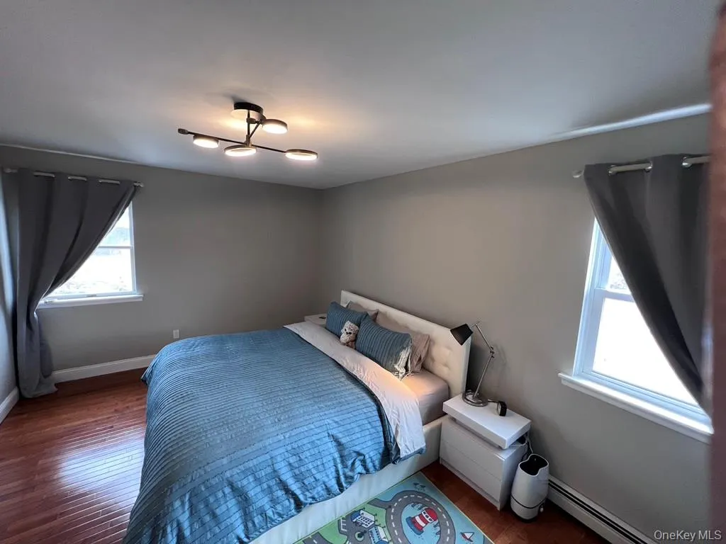 Second bedroom with california-king-size bed and hardwood flooring, light gray wall paint, and a modern ceiling light fixture, two windows allow cross-ventilation Second bedroom with california-king-size bed and hardwood flooring, light gray wall paint, and a modern ceiling light fixture, two windows allow cross-ventilation