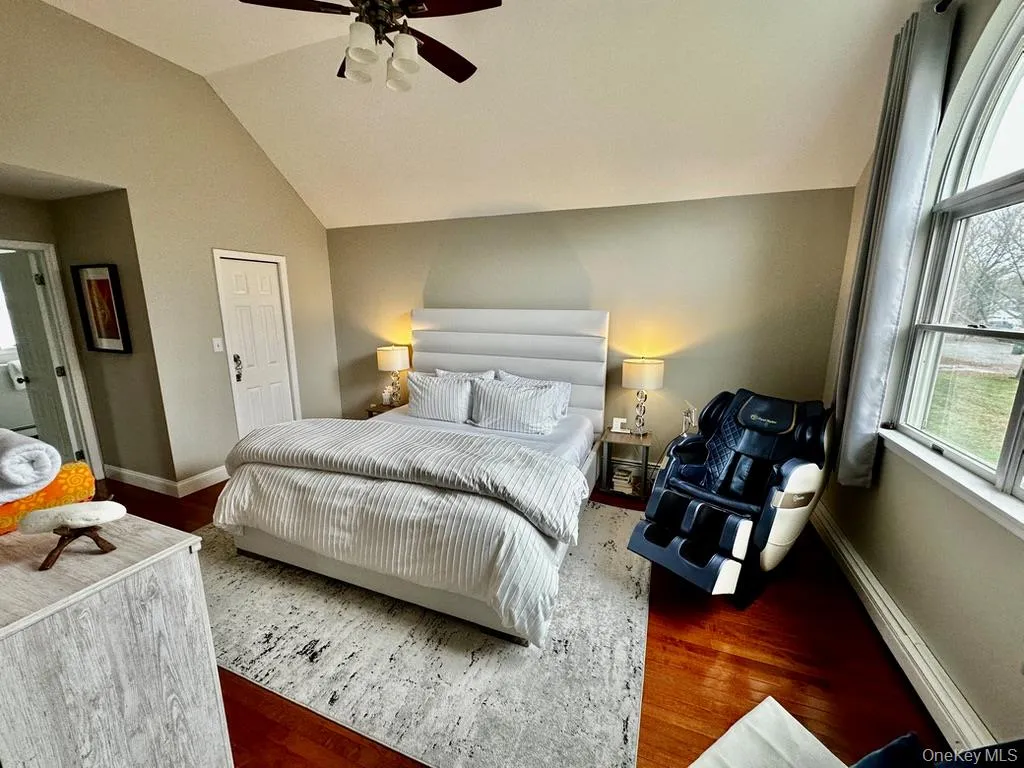 Primary room features vaulted ceiling, ceiling fan with integrated lighting, wood-finish flooring, and an arched window and a massage chair Primary room features vaulted ceiling, ceiling fan with integrated lighting, wood-finish flooring, and an arched window and a massage chair