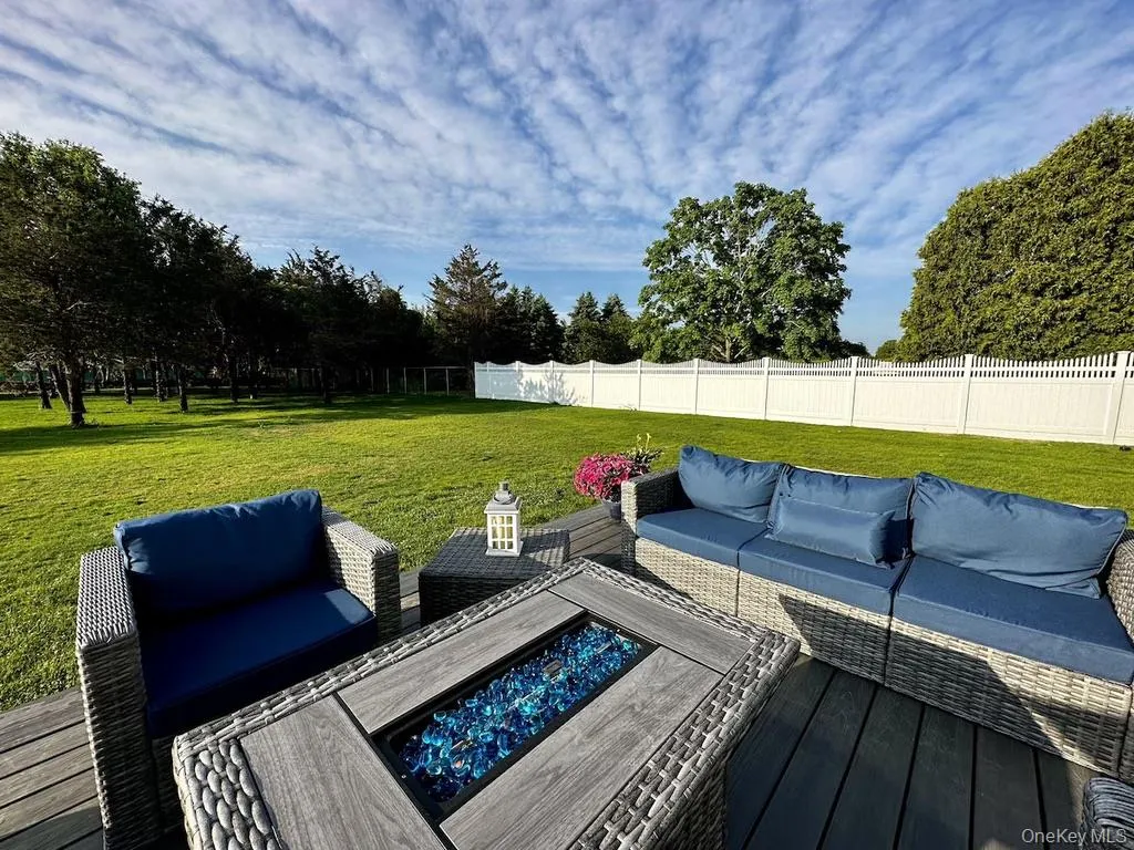 Expansive outdoor decking with a fire pit, overlooking a manicured lawn, mature trees, and a white privacy fence Expansive outdoor decking with a fire pit, overlooking a manicured lawn, mature trees, and a white privacy fence