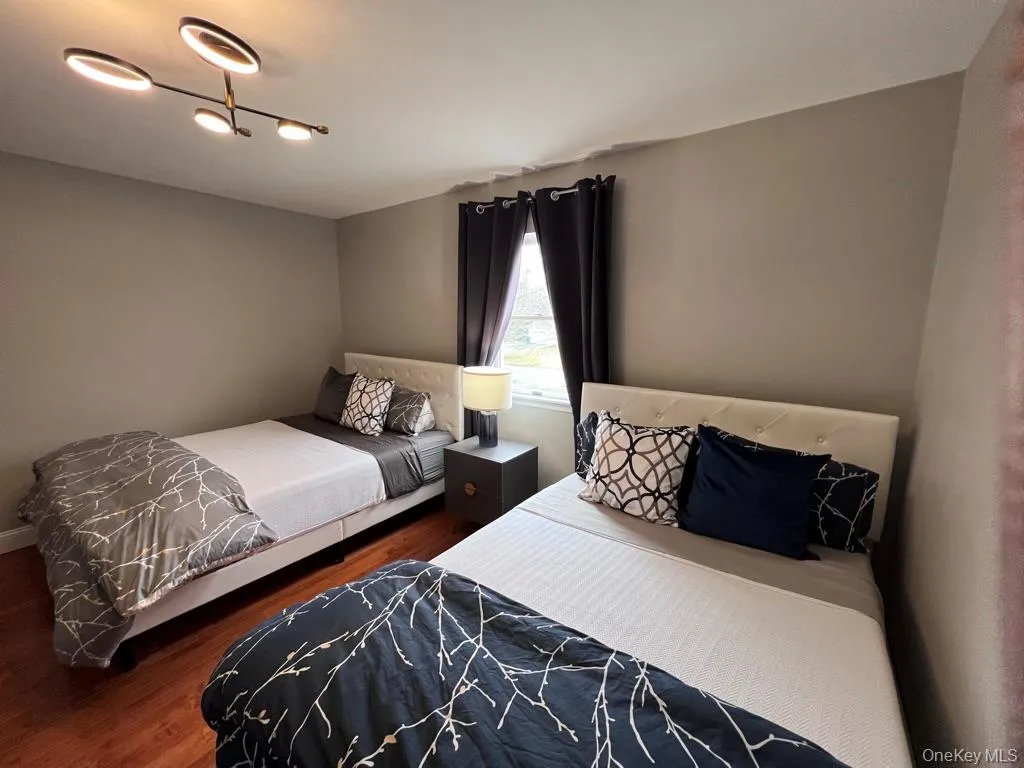 Third bedroom with two full size-beds and wood-finish flooring with neutral wall paint and a modern ceiling light fixture Third bedroom with two full size-beds and wood-finish flooring with neutral wall paint and a modern ceiling light fixture