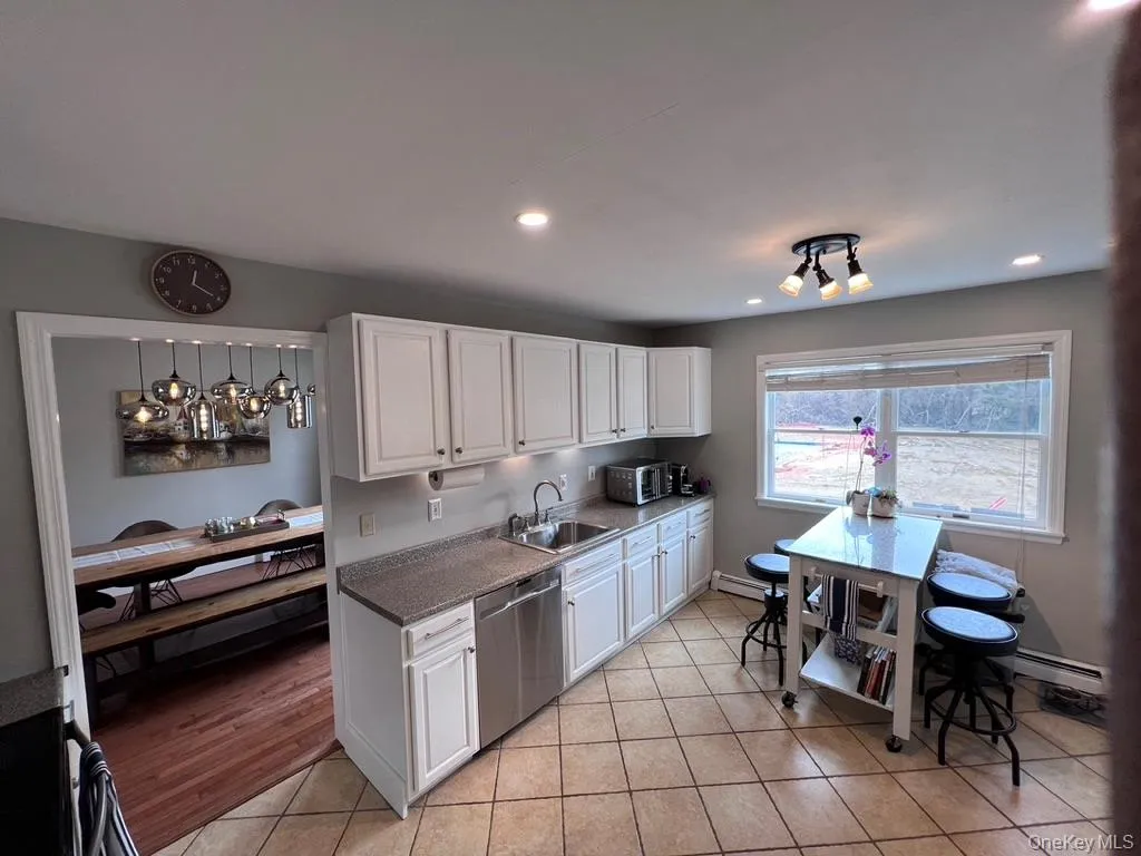 Kitchen featuring white cabinetry, stainless steel dishwasher, tile flooring, recessed lighting, and a large window facing backyard and view of swimming pool. Kitchen featuring white cabinetry, stainless steel dishwasher, tile flooring, recessed lighting, and a large window facing backyard and view of swimming pool.