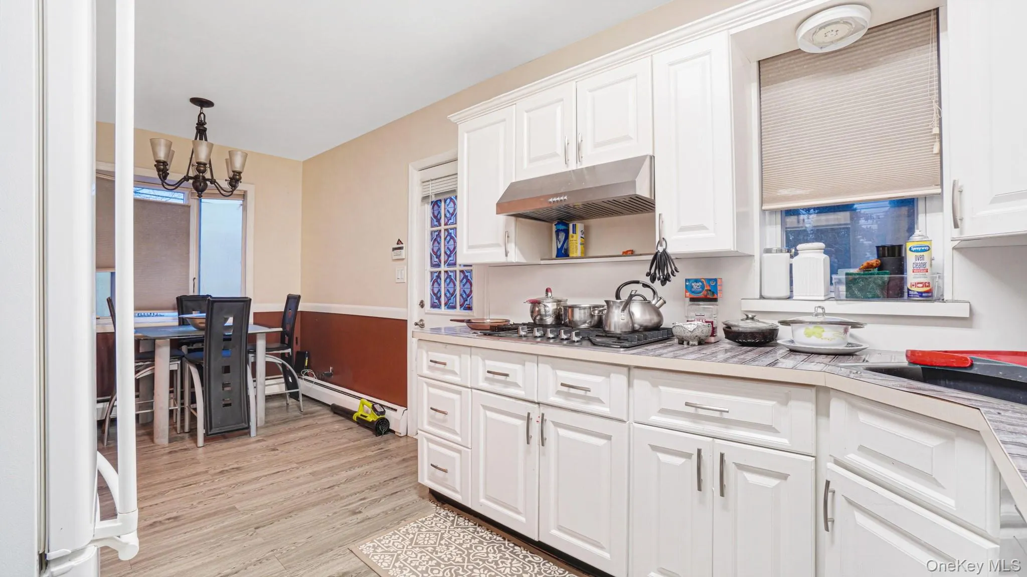 Kitchen featuring light countertops, white cabinetry, under cabinet range hood, and an inviting chandelier Kitchen featuring light countertops, white cabinetry, under cabinet range hood, and an inviting chandelier