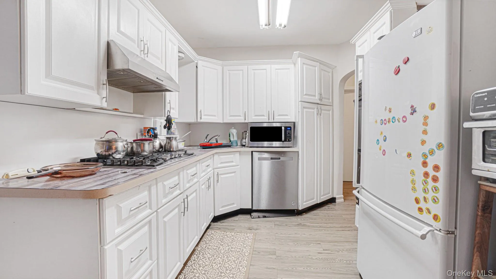 Kitchen featuring under cabinet range hood, light countertops, light wood-style floors, appliances with stainless steel finishes, and white cabinetry Kitchen featuring under cabinet range hood, light countertops, light wood-style floors, appliances with stainless steel finishes, and white cabinetry