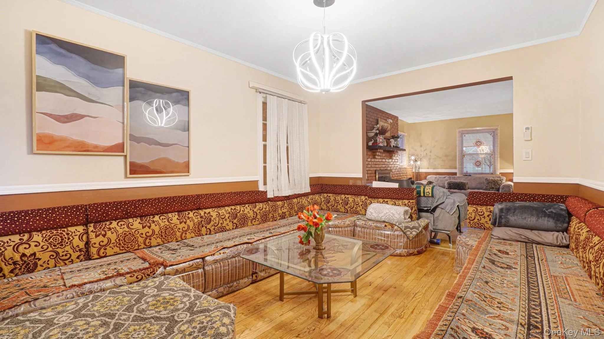 Living room with wood-type flooring, crown molding, a wainscoted wall, and a chandelier Living room with wood-type flooring, crown molding, a wainscoted wall, and a chandelier