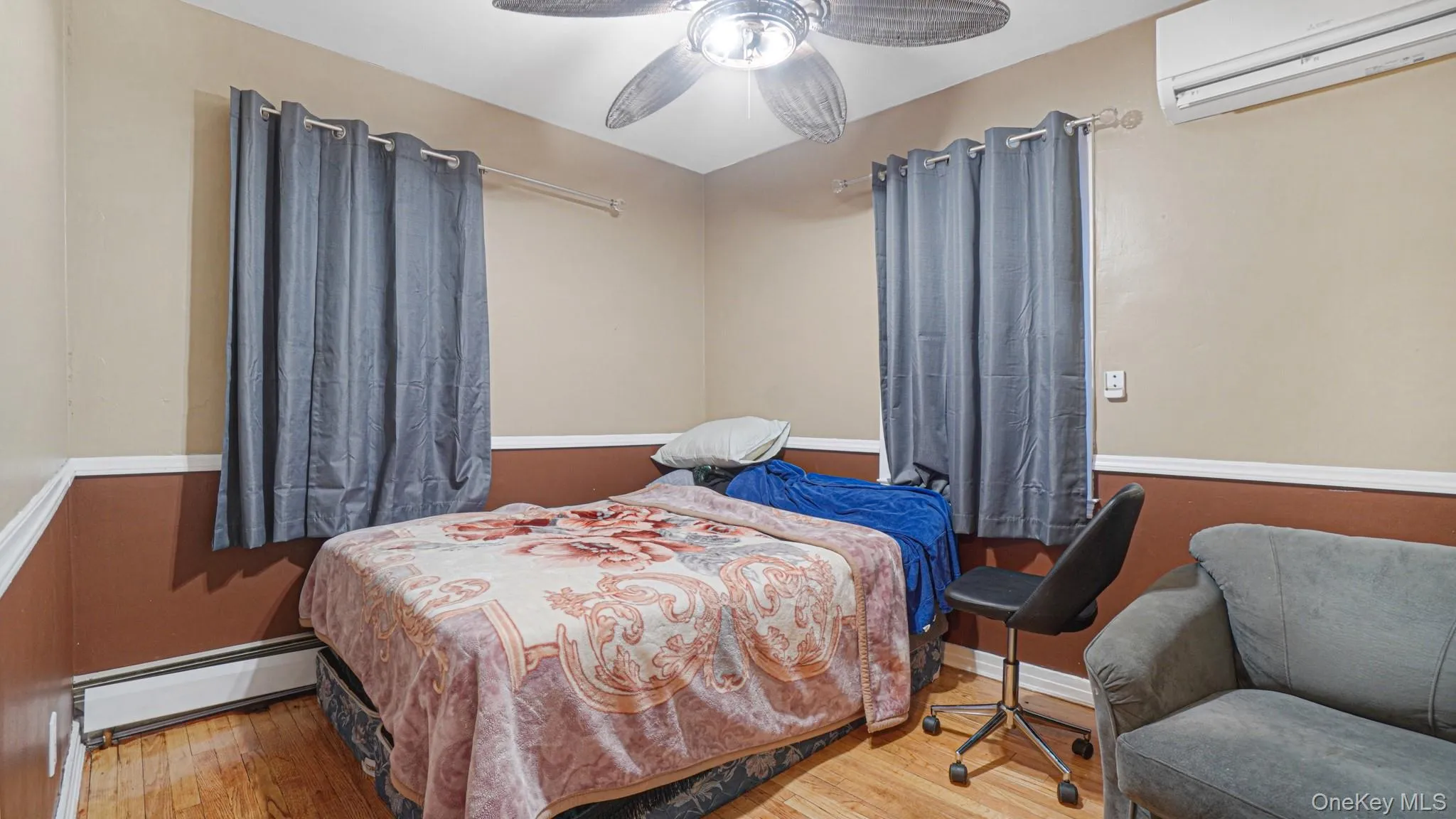 Bedroom featuring a baseboard heating unit, a ceiling fan, wood finished floors, and a wall mounted AC Bedroom featuring a baseboard heating unit, a ceiling fan, wood finished floors, and a wall mounted AC