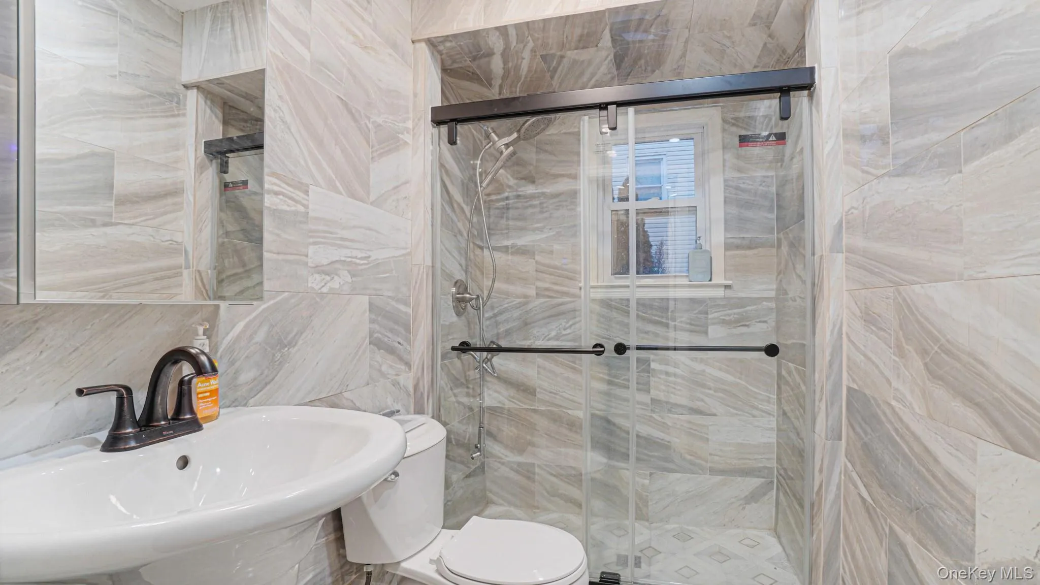 Bathroom with a shower stall, toilet, a sink, and tile walls Bathroom with a shower stall, toilet, a sink, and tile walls