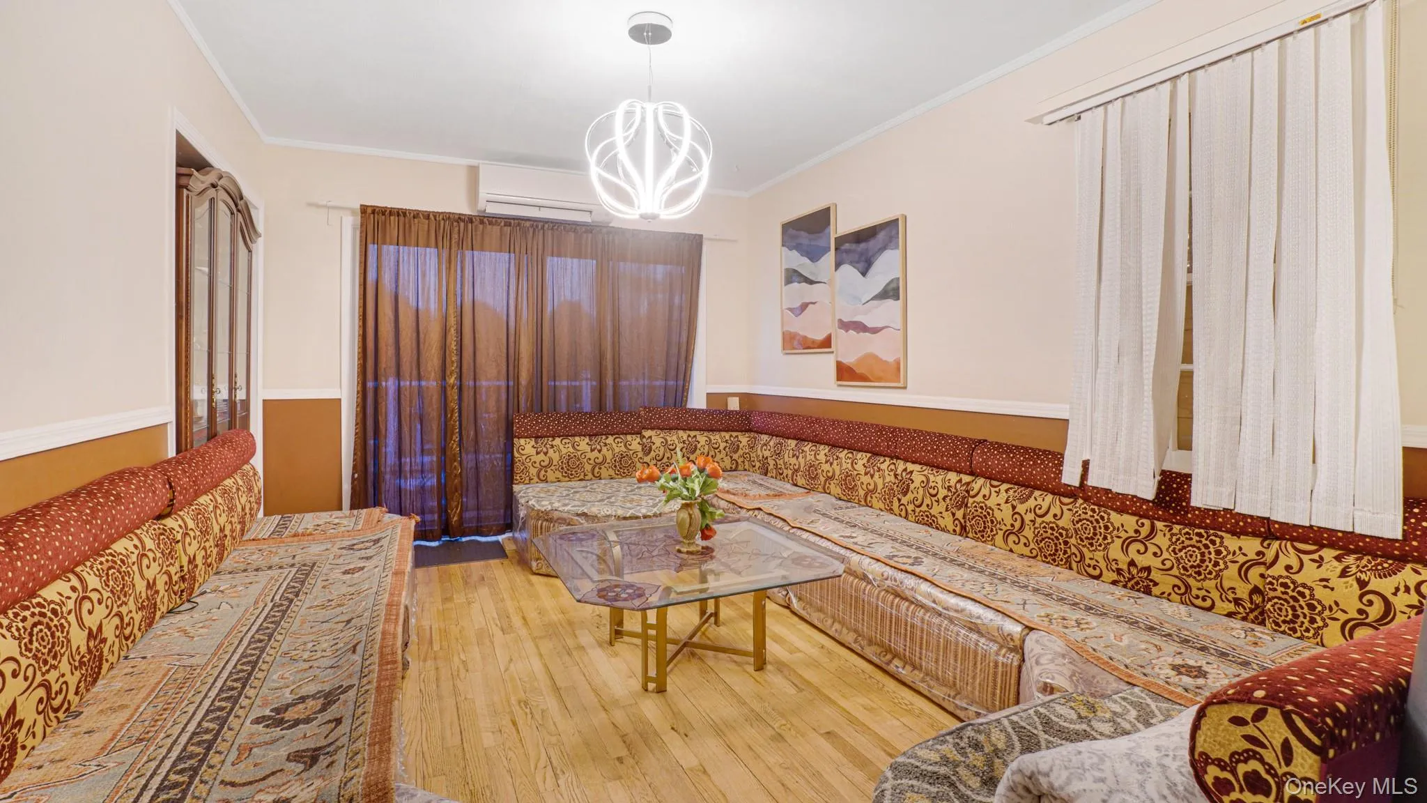 Living area featuring hardwood / wood-style flooring, an inviting chandelier, ornamental molding, and a wall mounted air conditioner Living area featuring hardwood / wood-style flooring, an inviting chandelier, ornamental molding, and a wall mounted air conditioner