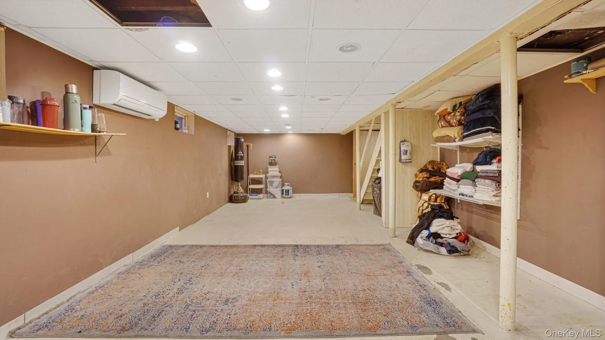 Finished below grade area featuring recessed lighting, a wall mounted air conditioner, baseboards, a paneled ceiling, and stairs Finished below grade area featuring recessed lighting, a wall mounted air conditioner, baseboards, a paneled ceiling, and stairs