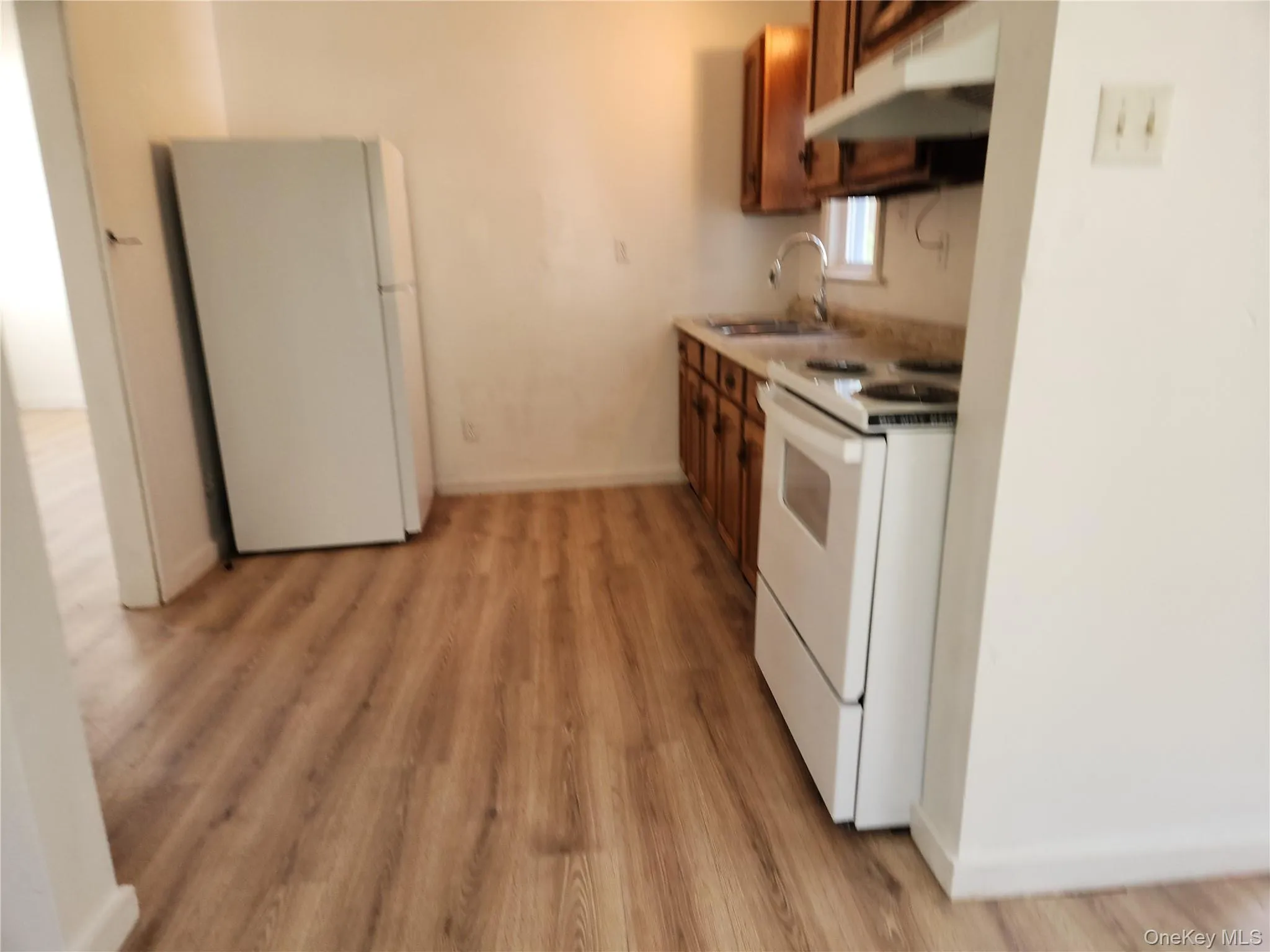 Kitchen featuring brown cabinets, a sink, white appliances, light wood-type flooring, and under cabinet range hood Kitchen featuring brown cabinets, a sink, white appliances, light wood-type flooring, and under cabinet range hood