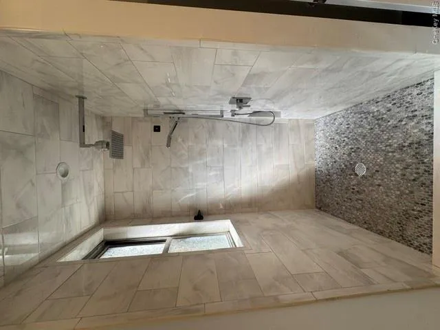 Oversized Walk-in shower featuring floor to ceiling wall tiles, a pebble-stone floor, rain shower head, and a hand-held shower fixture Oversized Walk-in shower featuring floor to ceiling wall tiles, a pebble-stone floor, rain shower head, and a hand-held shower fixture