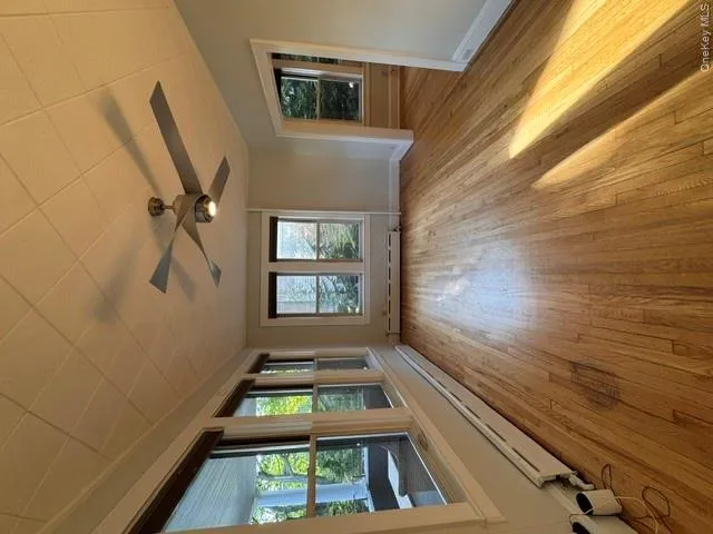 Spacious interior room featuring wood-finish flooring, multiple windows, a contemporary ceiling fan with integrated lighting, and crown molding Spacious interior room featuring wood-finish flooring, multiple windows, a contemporary ceiling fan with integrated lighting, and crown molding