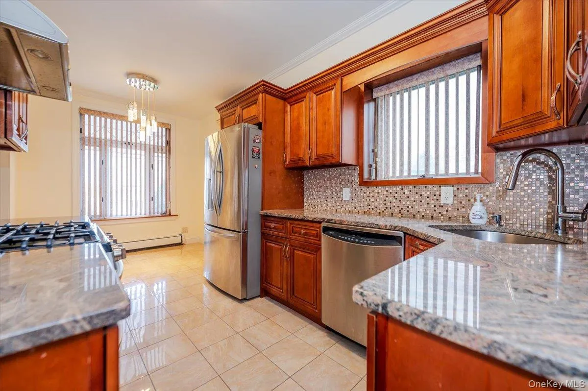 Kitchen featuring wood cabinetry, stainless steel appliances, granite countertops, and a mosaic tile backsplash Kitchen featuring wood cabinetry, stainless steel appliances, granite countertops, and a mosaic tile backsplash