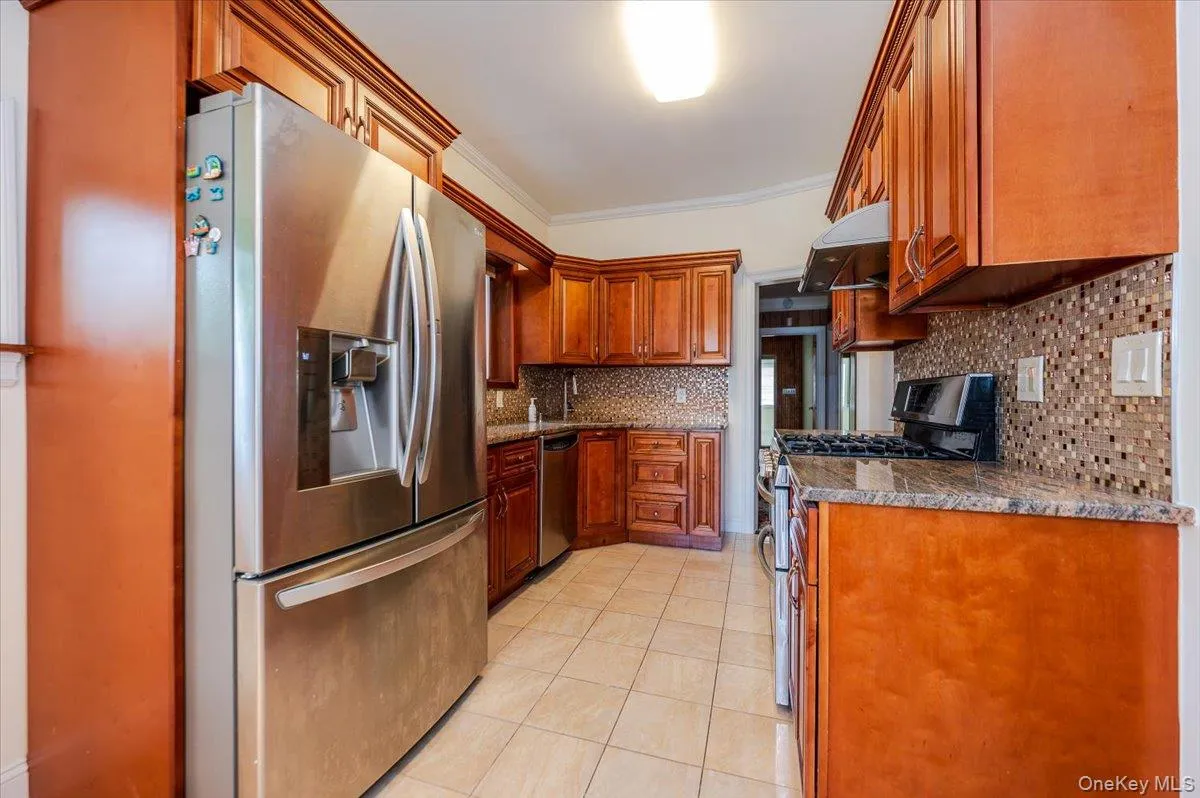 Kitchen featuring wood cabinetry, stainless steel appliances, mosaic tile backsplash, and stone countertops Kitchen featuring wood cabinetry, stainless steel appliances, mosaic tile backsplash, and stone countertops