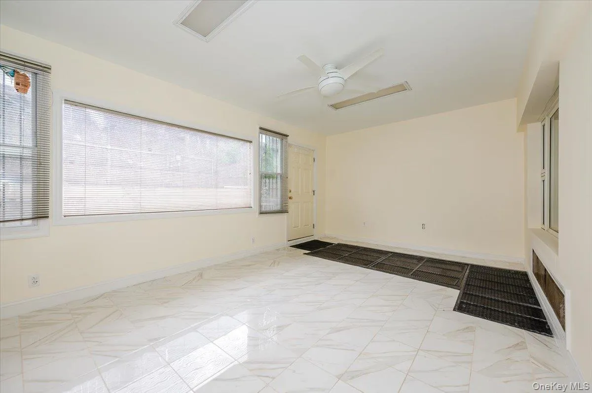 Spacious room featuring white marble-look tile flooring, light-toned walls, and a ceiling fan Spacious room featuring white marble-look tile flooring, light-toned walls, and a ceiling fan