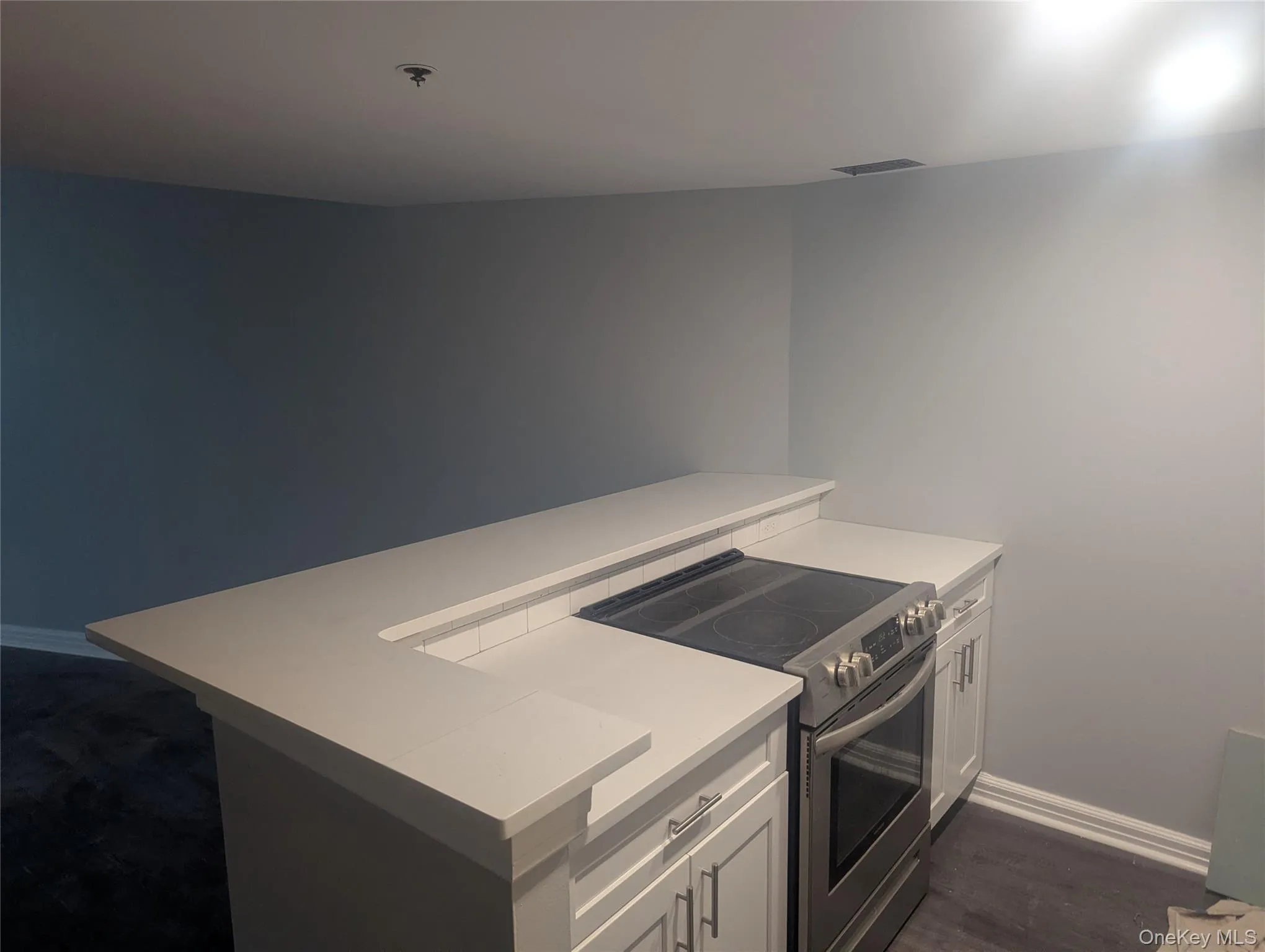 Kitchen island featuring a white countertop with a raised bar, white shaker-style cabinetry, and a stainless steel electric range Kitchen island featuring a white countertop with a raised bar, white shaker-style cabinetry, and a stainless steel electric range