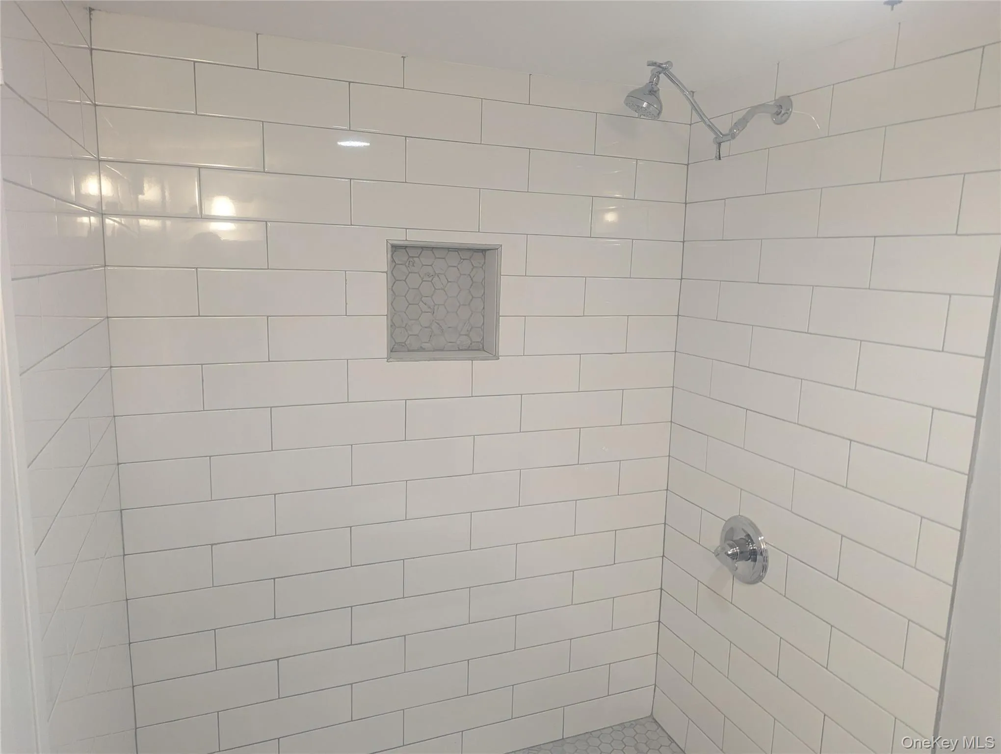 Shower stall featuring white subway tile walls, a built-in hexagonal mosaic tile niche, a chrome showerhead, and a chrome single-handle control Shower stall featuring white subway tile walls, a built-in hexagonal mosaic tile niche, a chrome showerhead, and a chrome single-handle control