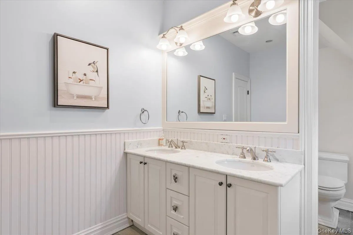Pristine full bathroom equipped with a wide double vanity and clean wainscoting paneling Pristine full bathroom equipped with a wide double vanity and clean wainscoting paneling