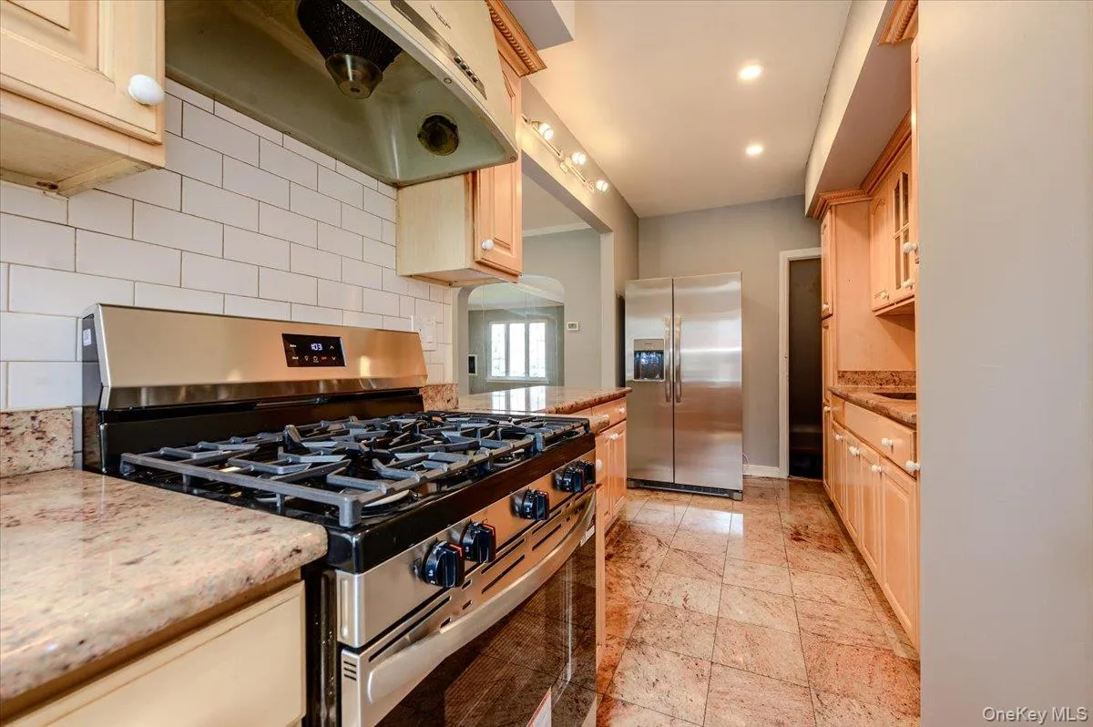 Stainless steel gas range, stainless steel refrigerator, light wood-finish cabinetry, subway tile backsplash, and stone-finish flooring Stainless steel gas range, stainless steel refrigerator, light wood-finish cabinetry, subway tile backsplash, and stone-finish flooring