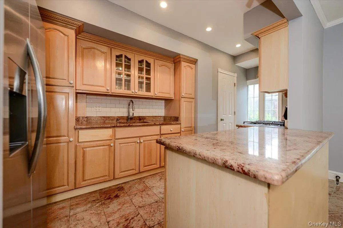 Recessed lighting illuminates the kitchen featuring wood cabinetry, a tile backsplash, and stone countertops Recessed lighting illuminates the kitchen featuring wood cabinetry, a tile backsplash, and stone countertops