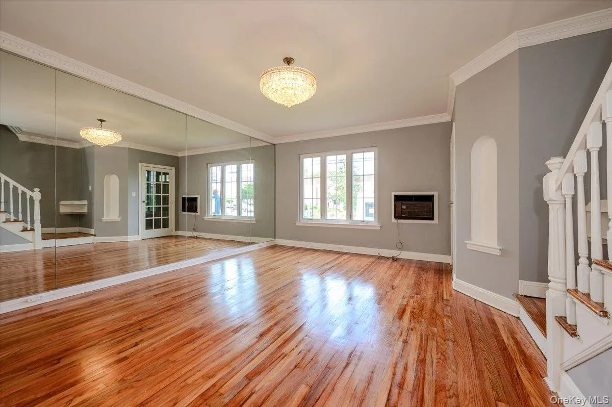 Expansive room featuring rich wood flooring, a full mirrored wall, and a staircase with white balusters Expansive room featuring rich wood flooring, a full mirrored wall, and a staircase with white balusters