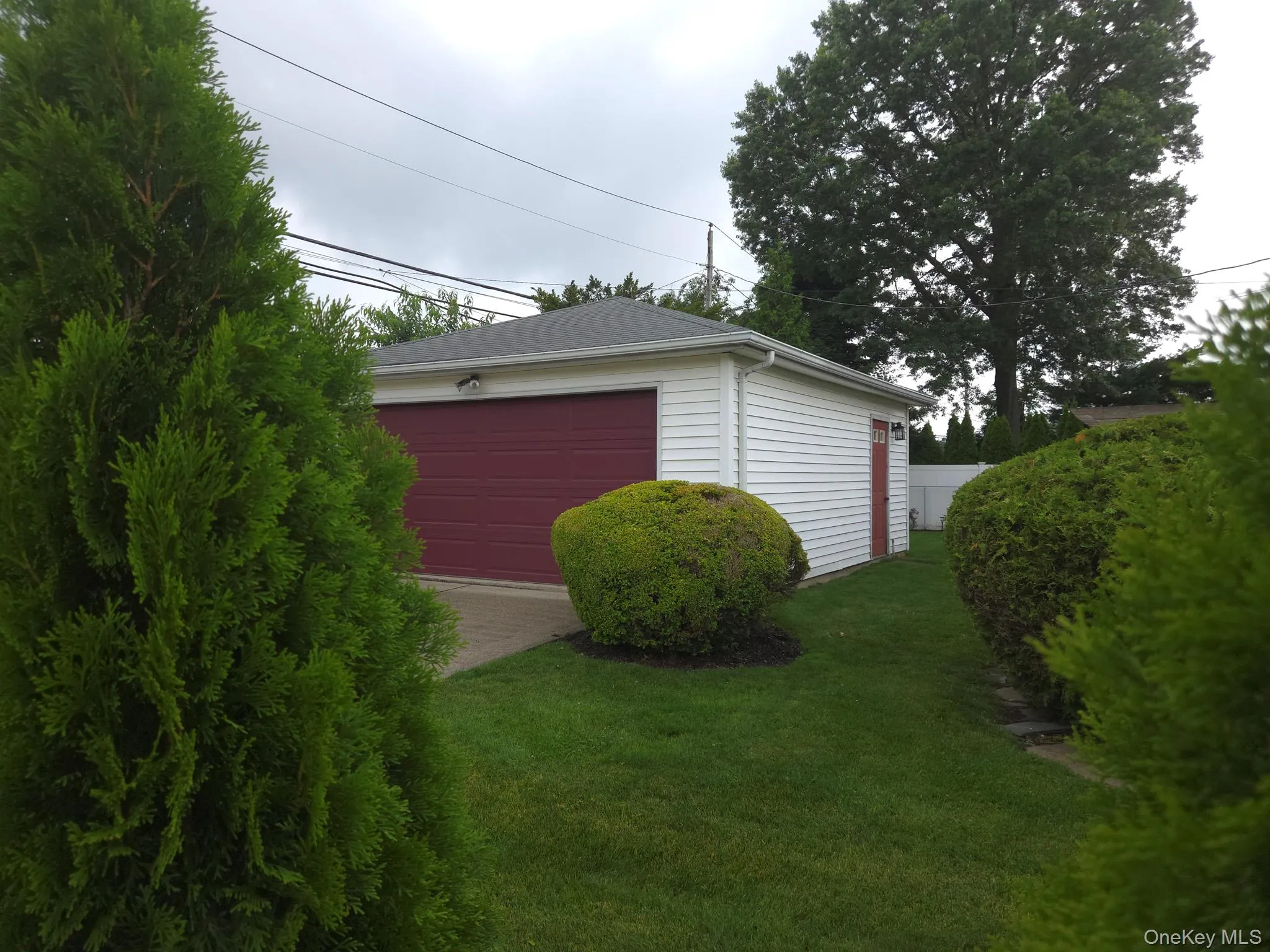 Detached 2 car garage featuring white horizontal siding, a dark red garage door, and a coordinating dark red side door Detached 2 car garage featuring white horizontal siding, a dark red garage door, and a coordinating dark red side door