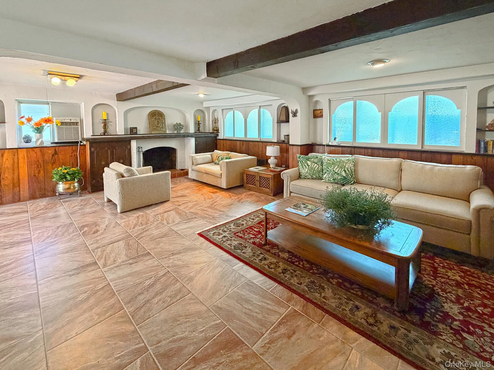 Spacious room featuring tile flooring, exposed wood ceiling beams, a WBFPL and wood paneling on lower walls Spacious room featuring tile flooring, exposed wood ceiling beams, a WBFPL and wood paneling on lower walls