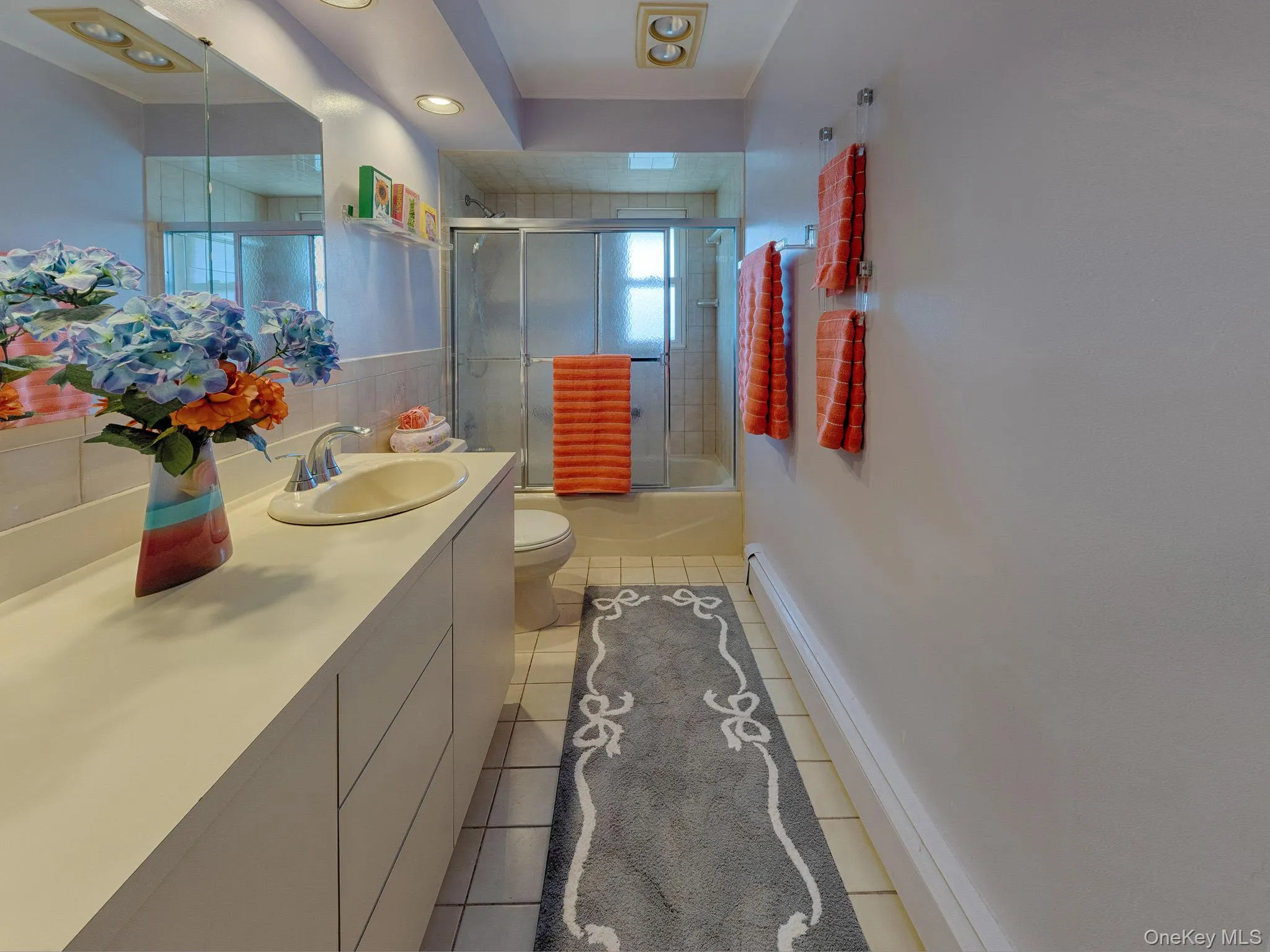 Bathroom featuring an integrated vanity sink, extensive countertop space, a tub with glass enclosure and a full-width mirror Bathroom featuring an integrated vanity sink, extensive countertop space, a tub with glass enclosure and a full-width mirror