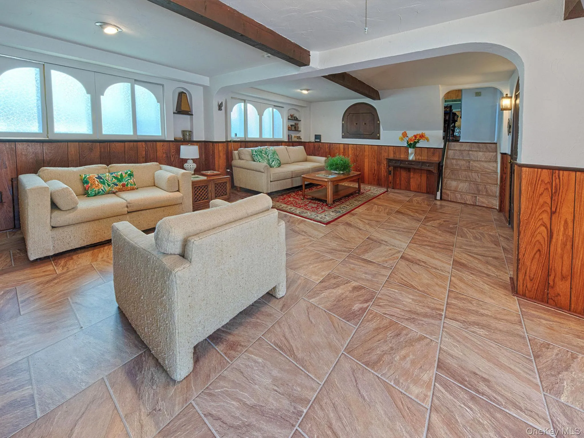 Spacious living area featuring large format tile flooring and wood paneling Spacious living area featuring large format tile flooring and wood paneling