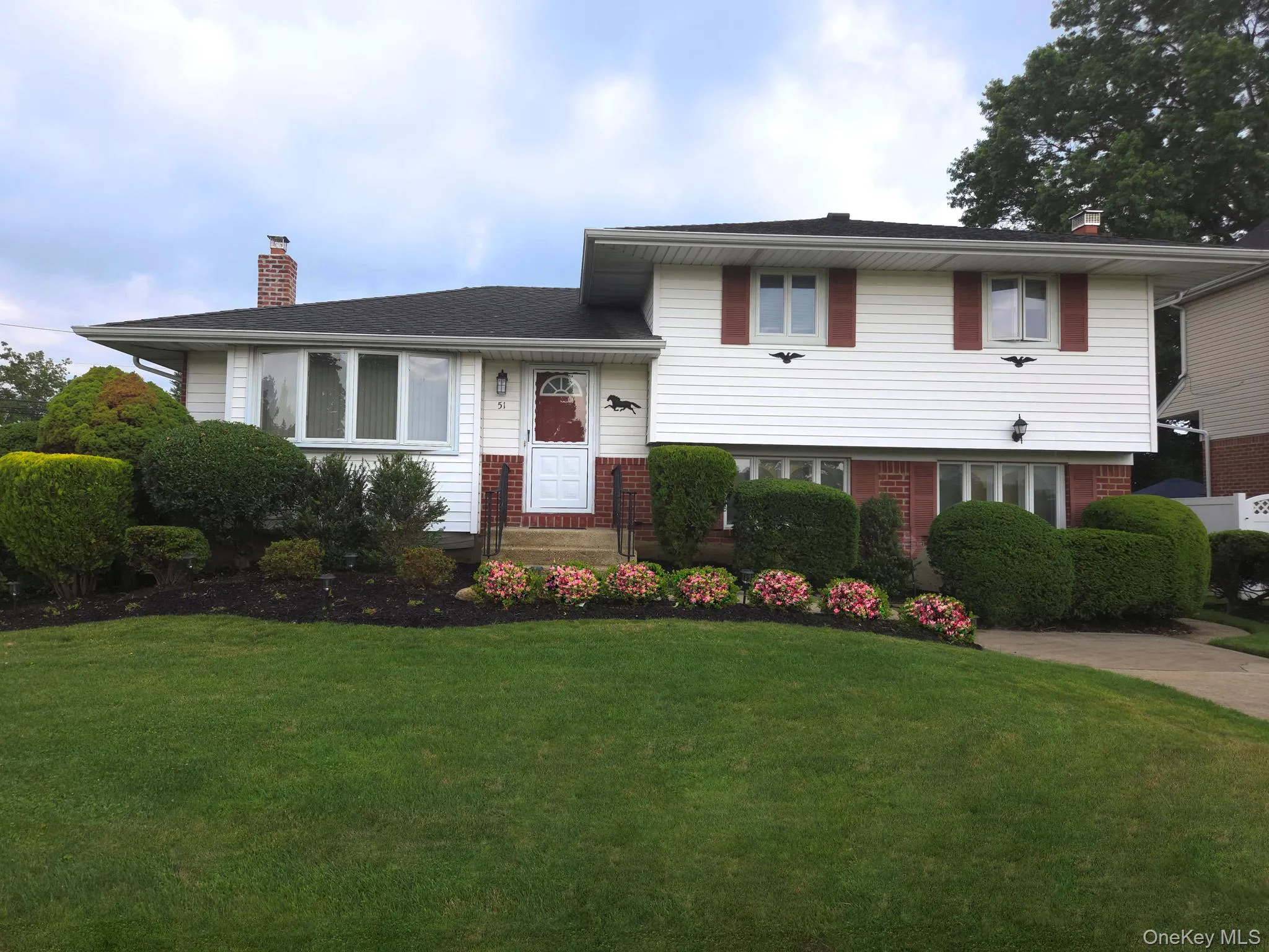 Split-level residence featuring white siding, a dark shingle roof, and a red front door Split-level residence featuring white siding, a dark shingle roof, and a red front door