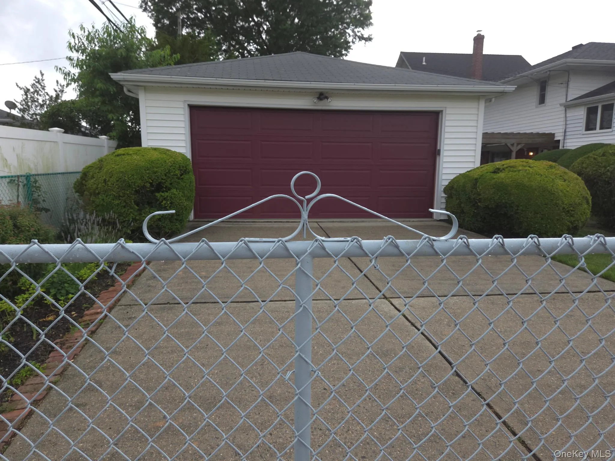 Detached and gated 2 car garage featuring white horizontal siding, a dark red garage door, dark red side door and gabled roof Detached and gated 2 car garage featuring white horizontal siding, a dark red garage door, dark red side door and gabled roof