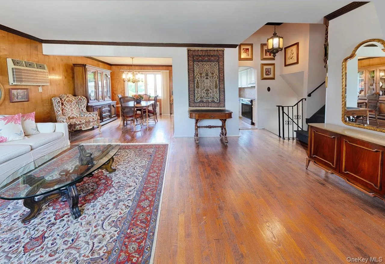 Hardwood flooring spans the main living area, featuring a dining space with a chandelier and a kitchen beyond Hardwood flooring spans the main living area, featuring a dining space with a chandelier and a kitchen beyond