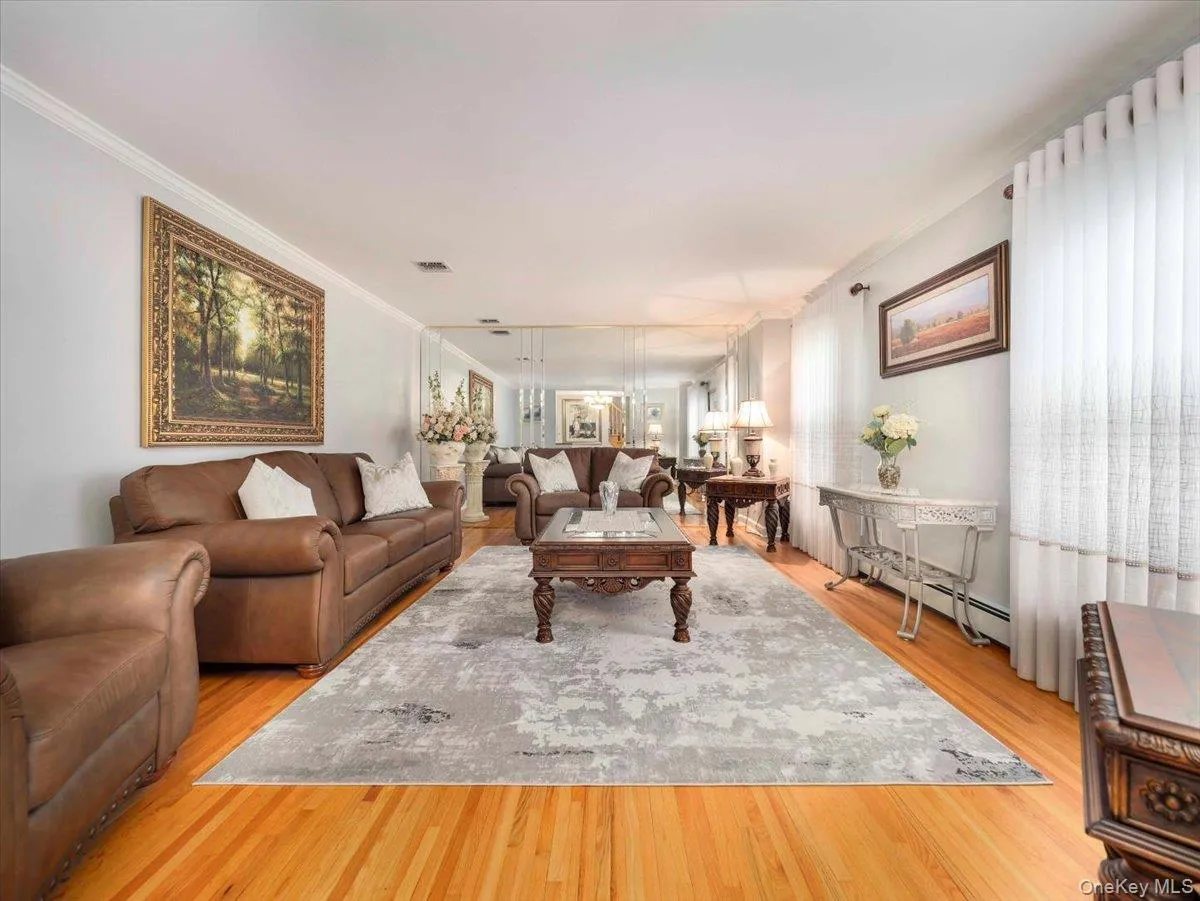 Spacious living area featuring polished wood-finish flooring, a decorative area rug, mirrored wall paneling, and crown molding Spacious living area featuring polished wood-finish flooring, a decorative area rug, mirrored wall paneling, and crown molding