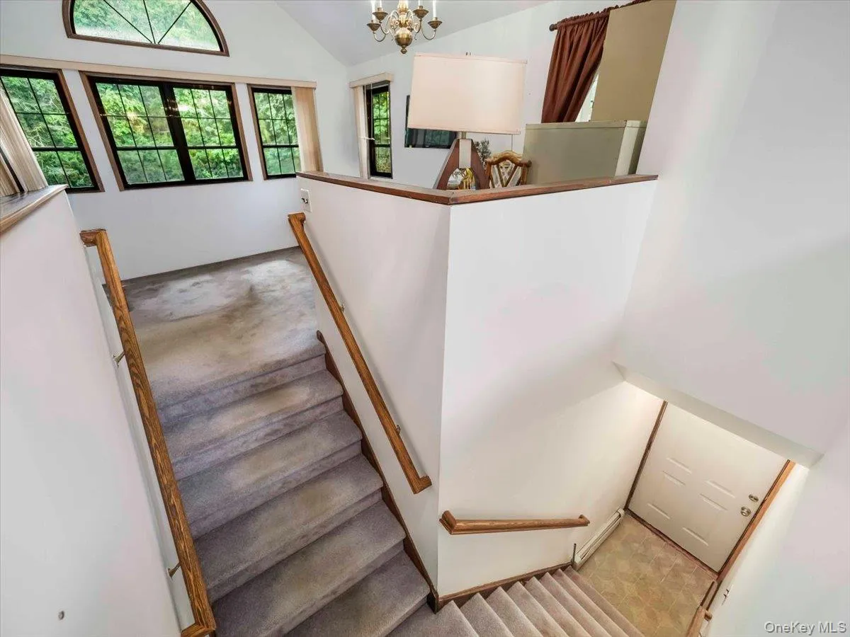Multi-level interior featuring a carpeted staircase with wood railings, a vaulted ceiling, and multiple windows with dark frames Multi-level interior featuring a carpeted staircase with wood railings, a vaulted ceiling, and multiple windows with dark frames