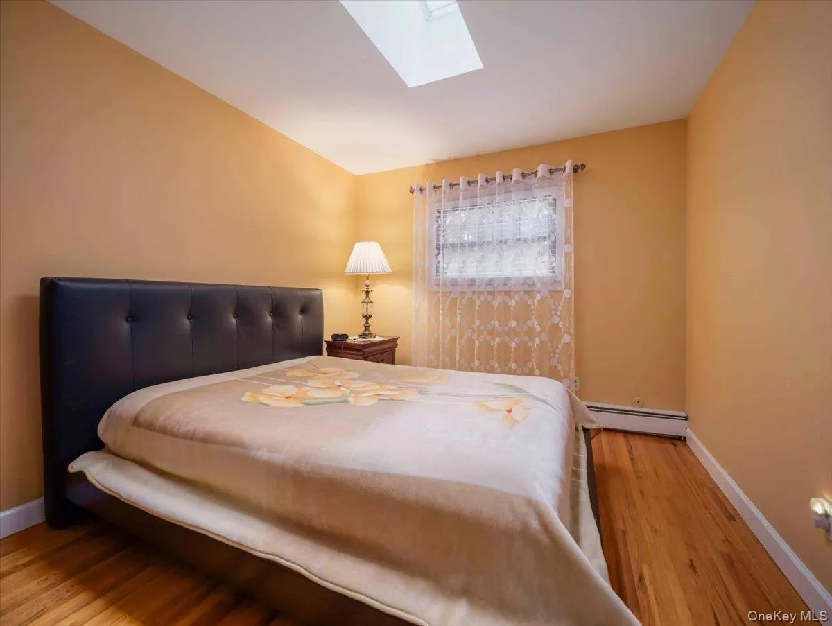 Bedroom featuring a skylight, wood-finish flooring, and a window with white trim Bedroom featuring a skylight, wood-finish flooring, and a window with white trim